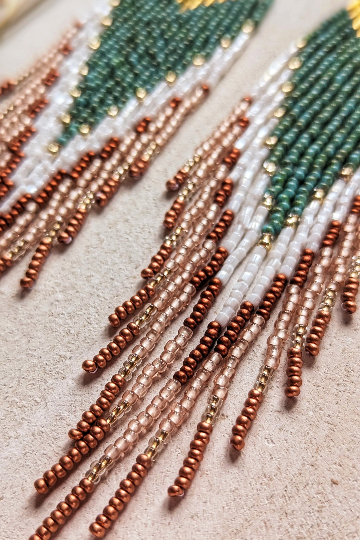 Close-up of handcrafted Moon & Milk earrings with turquoise, white, and crimson beads arranged in a chevron pattern, hanging from brass diamond-shaped findings.