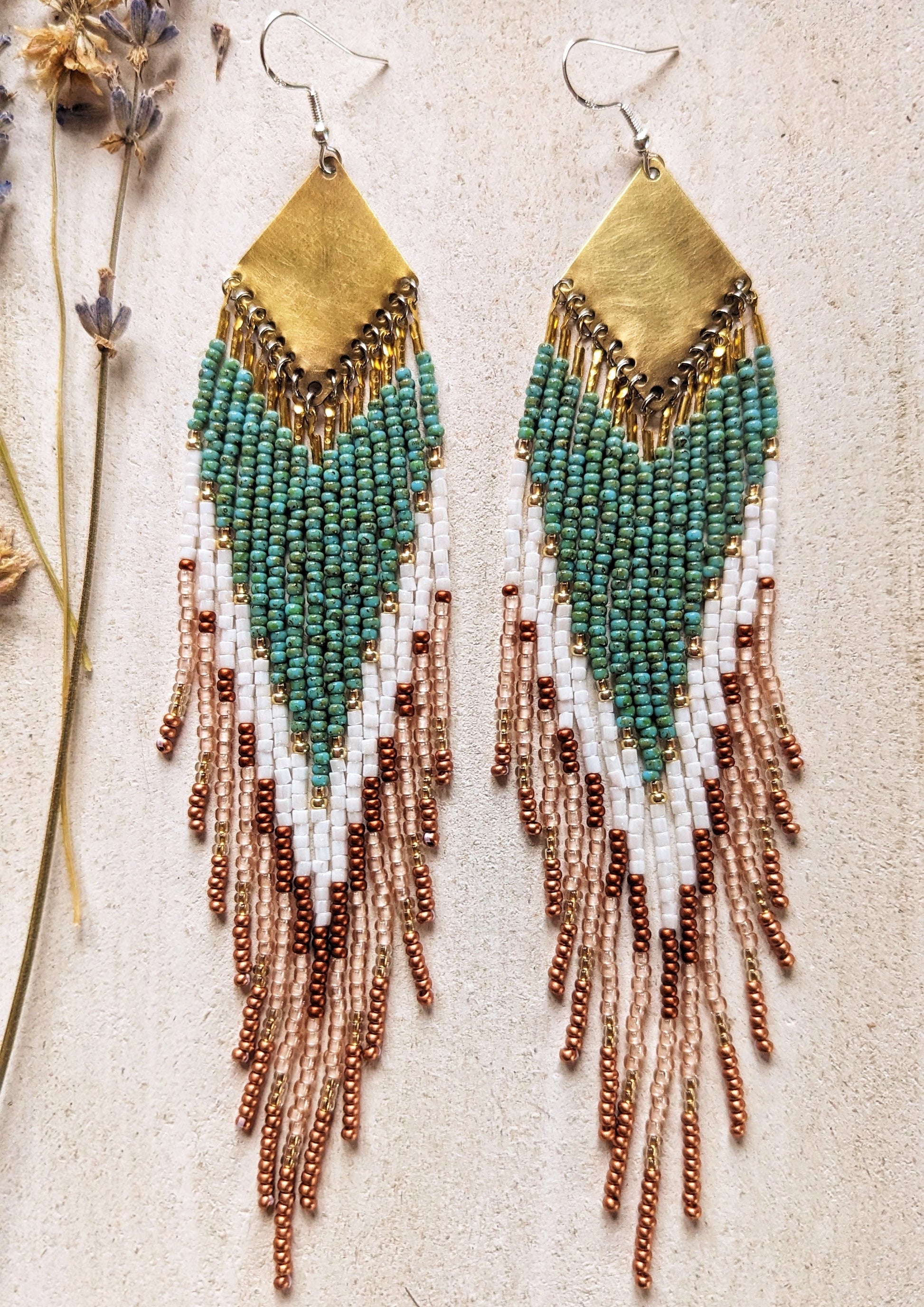 Handcrafted Moon & Milk earrings with turquoise, white, and crimson beads arranged in a chevron pattern, hanging from brass diamond-shaped findings.
