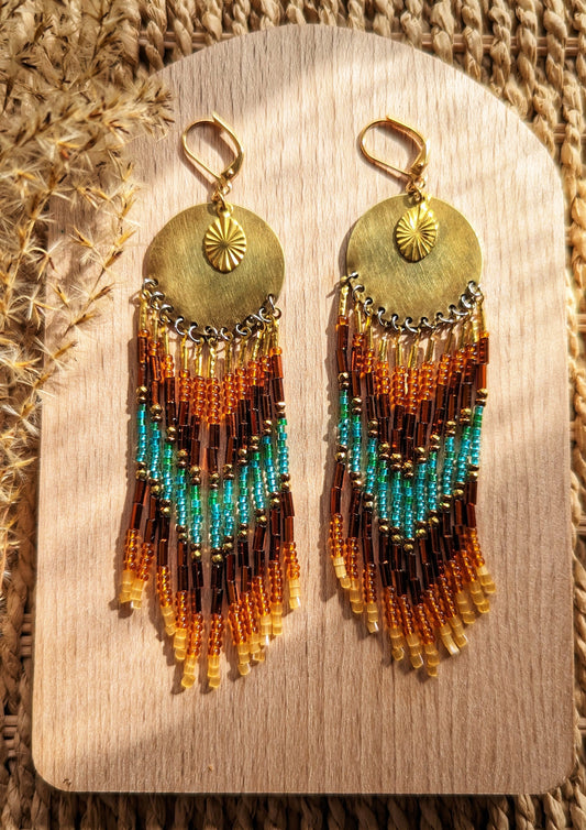 Moon & Milk boho earrings with gold sunburst discs, amber and turquoise seed beads, and bronze bugles, styled on wood with dried grasses.