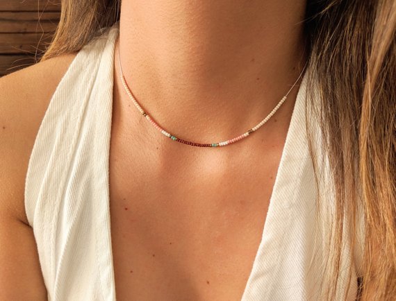 Close-up of a delicate beaded choker necklace with pastel pink, turquoise, and cream beads, styled elegantly on a woman wearing a white top.