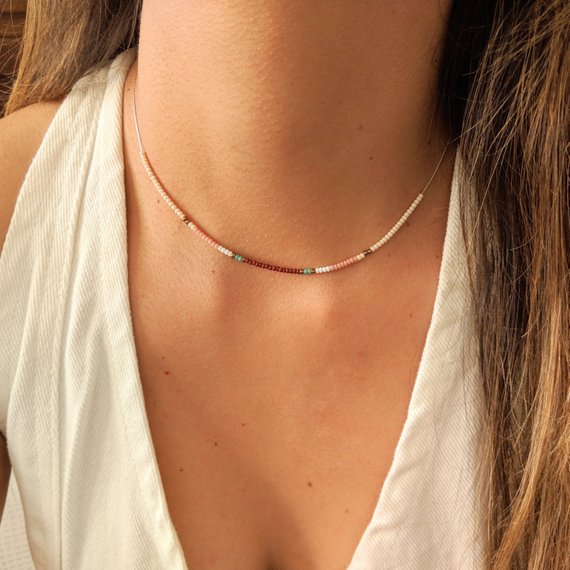 Close-up of a delicate beaded choker necklace with pastel pink, turquoise, and cream beads, styled elegantly on a woman wearing a white top.