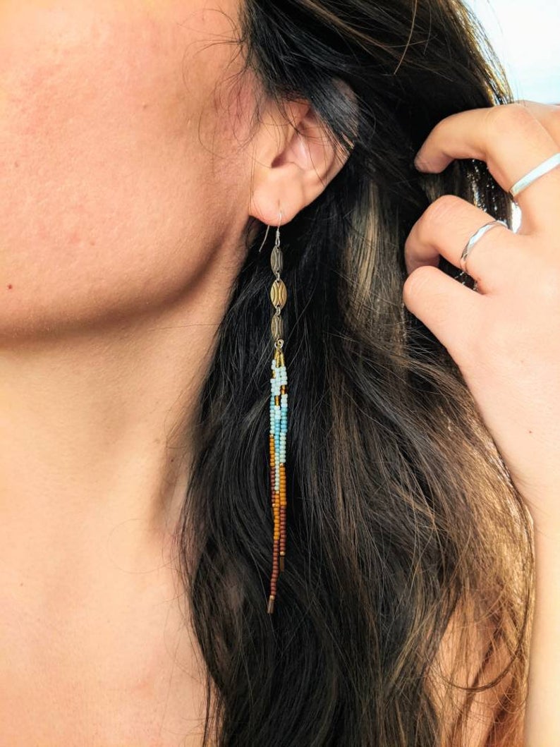 Moon & Milk artisan earrings with blue, cream, and rust-toned beads, accented with antique brass ovals, shown worn against long dark hair.
