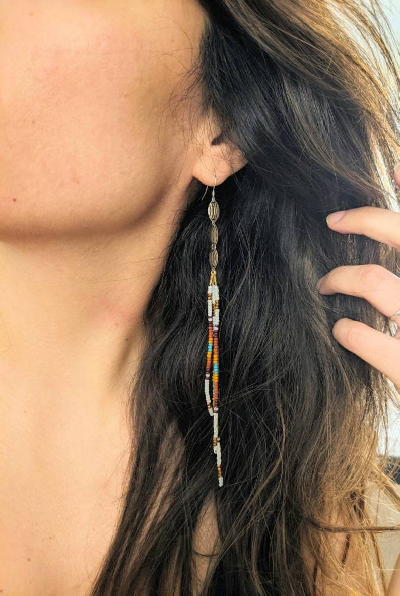Moon & Milk - Model wearing long, multicolored beaded earrings with a mix of white, brown, orange, and turquoise beads, featuring gold accents, showcasing a chic boho look against dark, wavy hair.