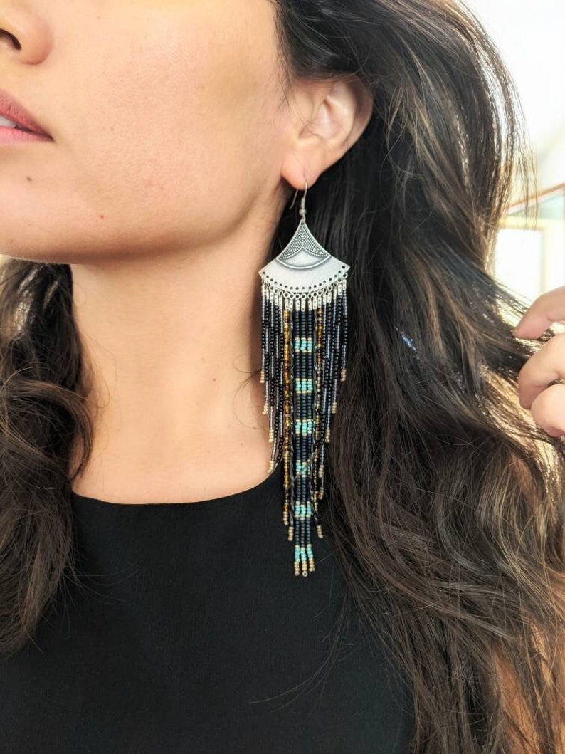 Moon & Milk long black and blue beaded earrings with silver fan tops and metallic accents, worn by a woman.