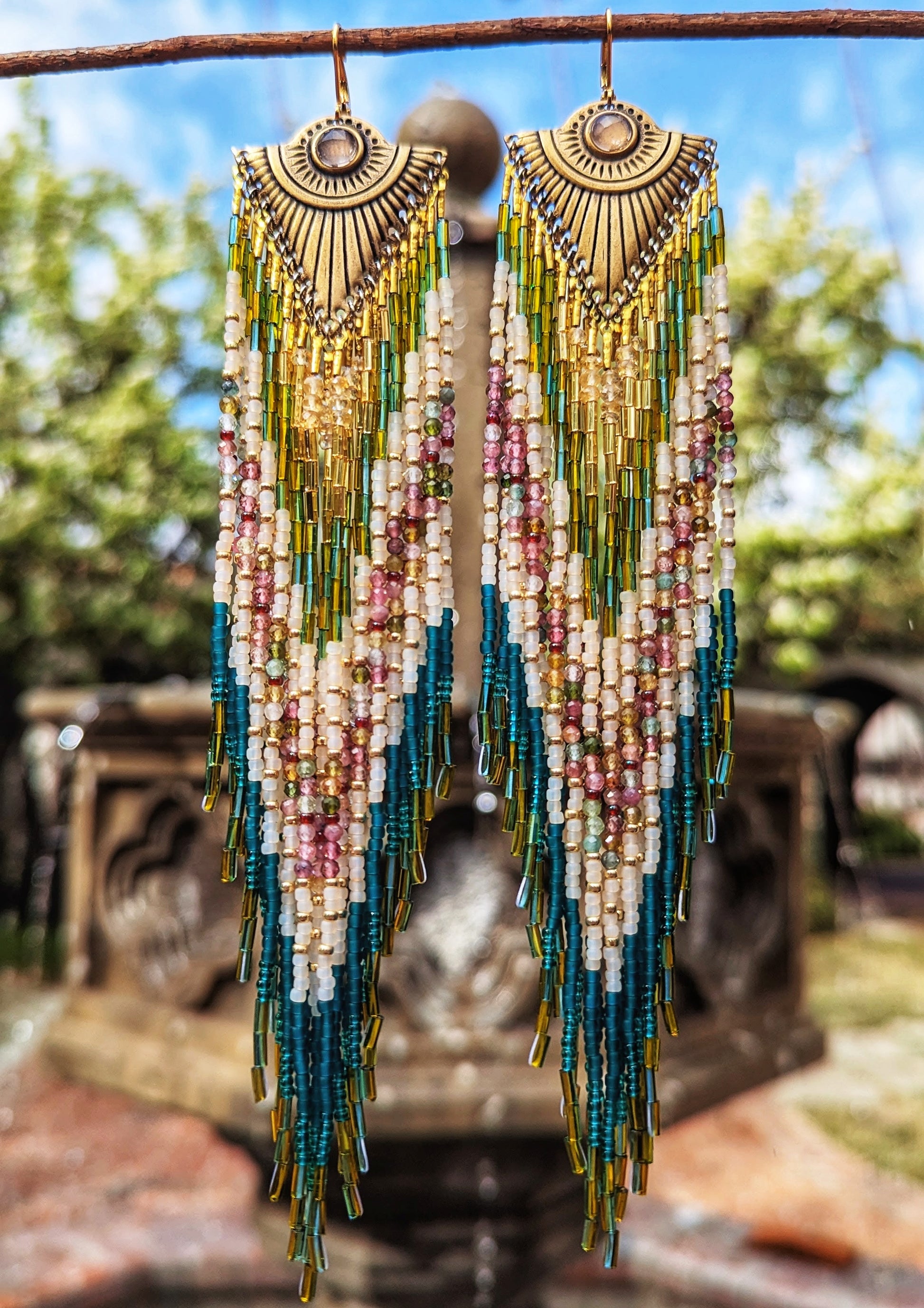 Handcrafted Moon & Milk beaded earrings honoring Xochipilli, with teal, gold, mauve, and watermelon tourmaline beadwork flowing from engraved brass fans.