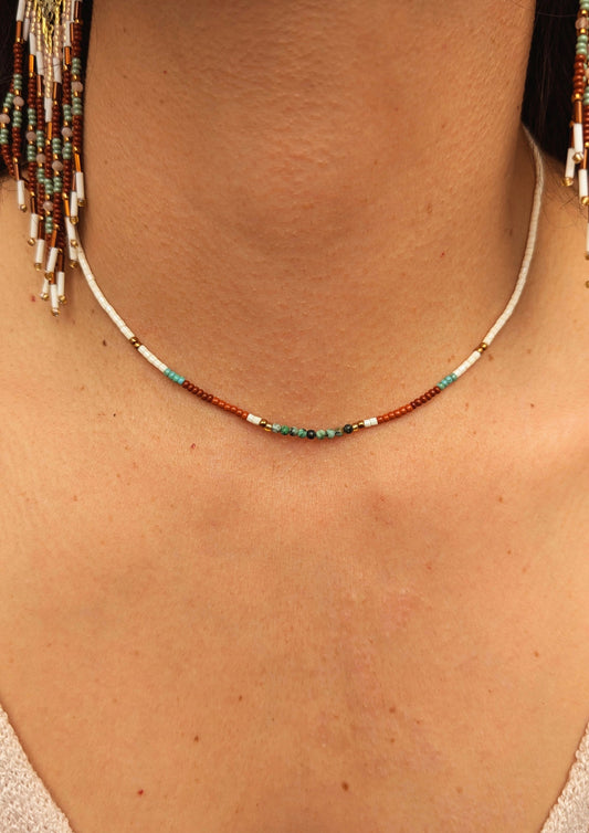 Moon & Milk - Woman wearing a delicate beaded choker necklace with white, brown, and turquoise beads. Close-up of the neck, highlighting the jewelry.