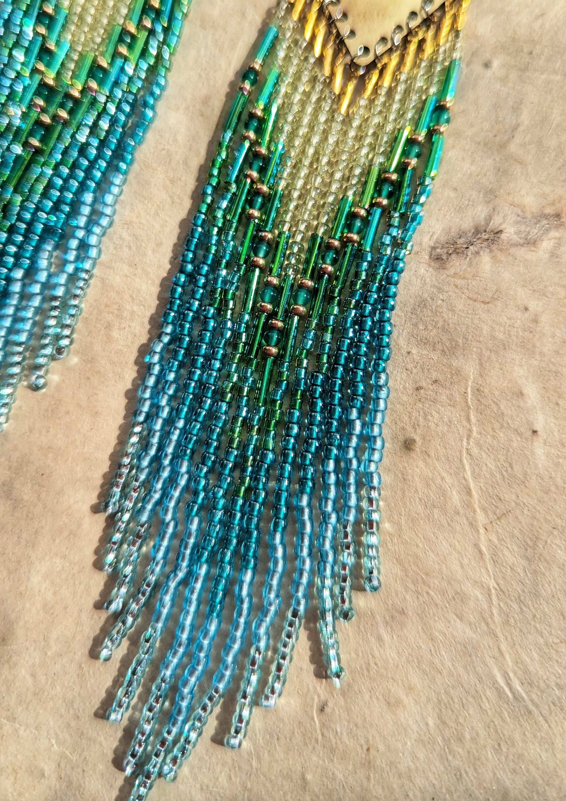 Moon & Milk - Handcrafted seed bead earrings in oceanic shades of blue and green, elegantly dangling from a brass diamond-shaped plate, beautifully contrasted against a light background.