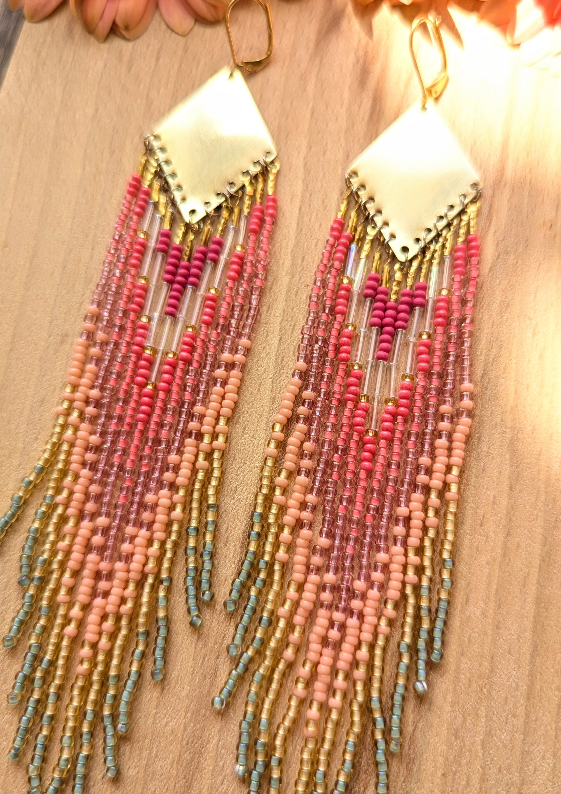 Moon & Milk - Vibrant handmade seed bead earrings featuring a blend of pink, peach, and mint green hues, cascading from a brass diamond plate, set against a natural background with soft pink flowers.