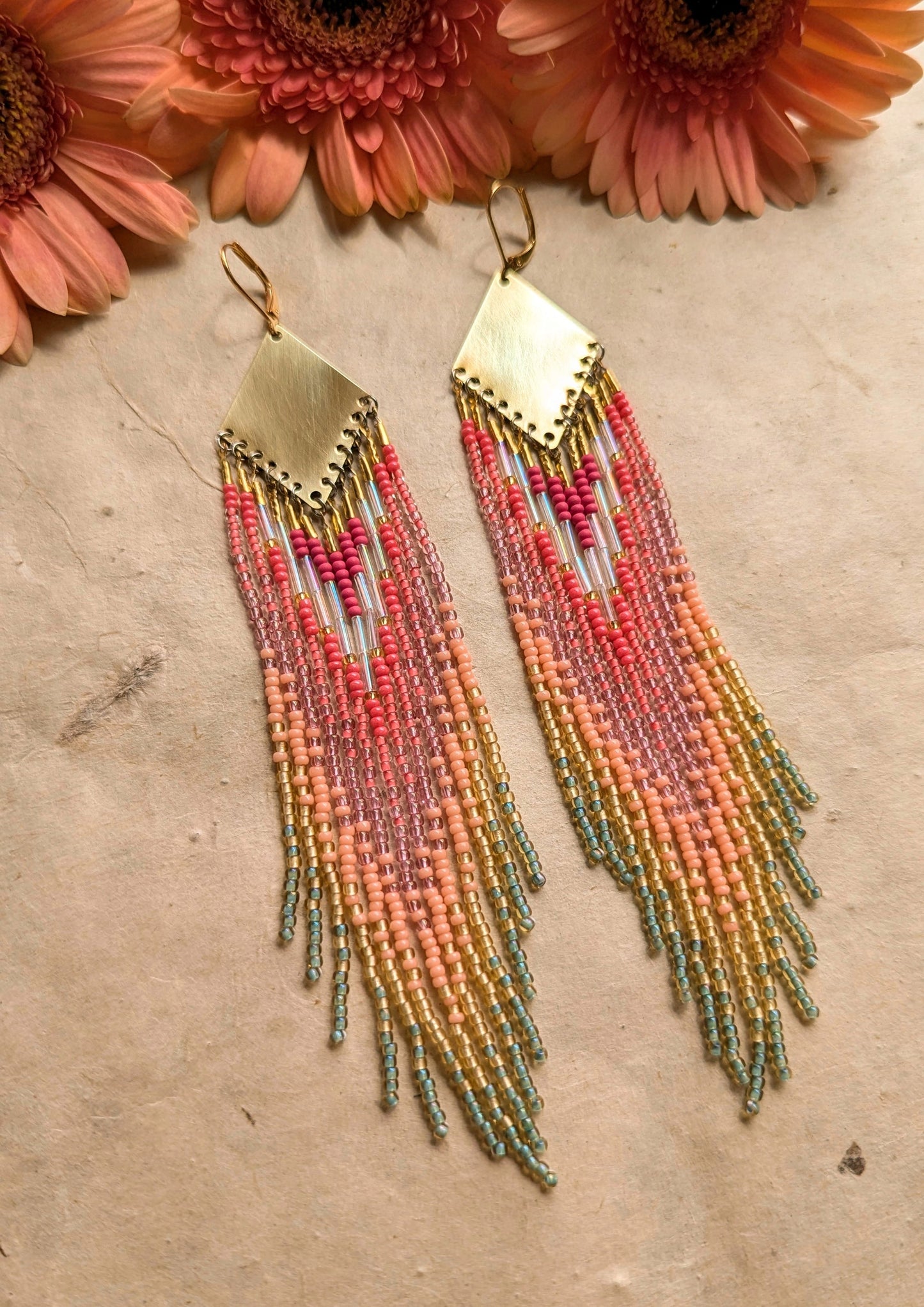 Moon & Milk - Vibrant handmade seed bead earrings featuring a blend of pink, peach, and mint green hues, cascading from a brass diamond plate, set against a natural background with soft pink flowers.