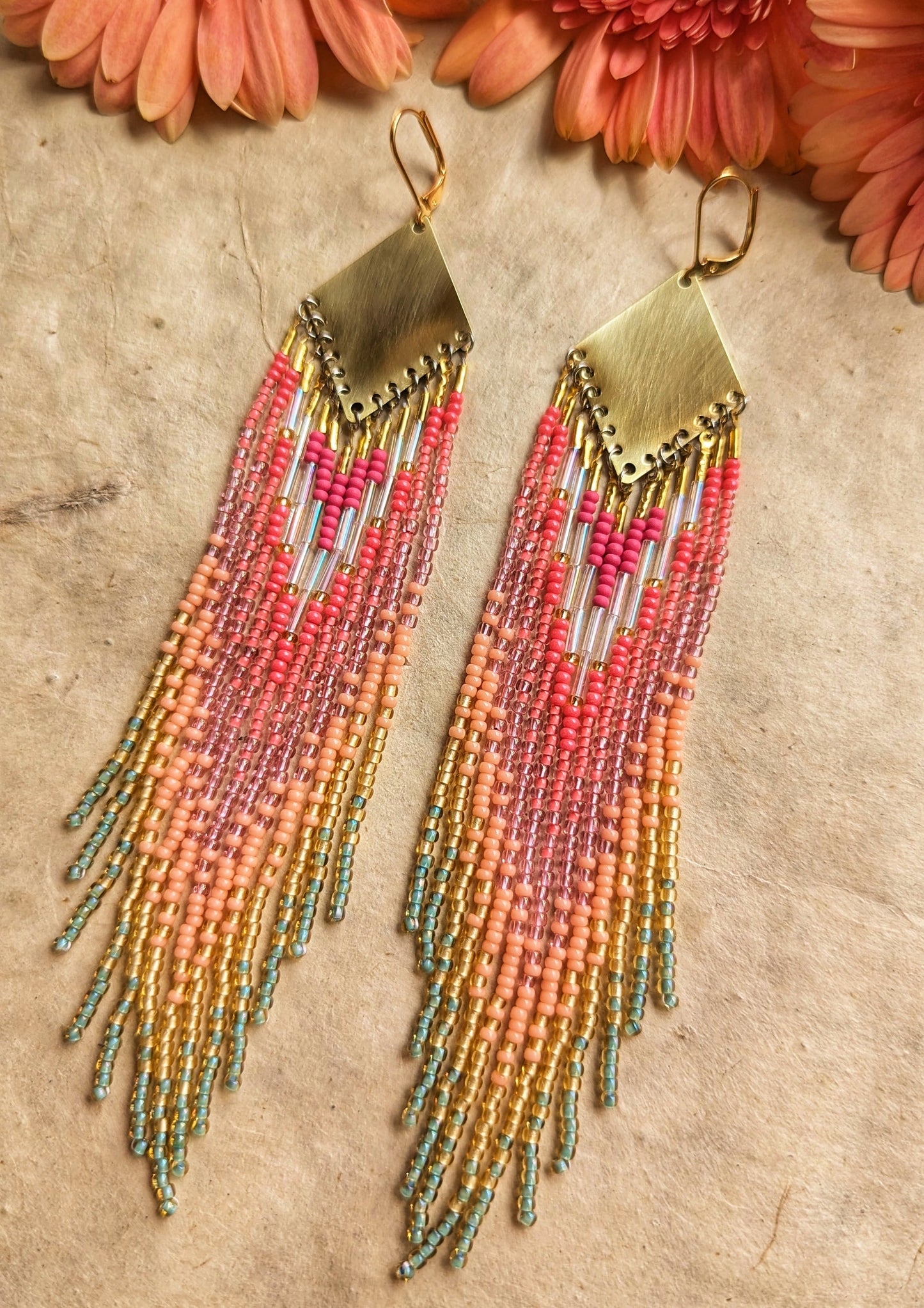 Moon & Milk - Vibrant handmade seed bead earrings featuring a blend of pink, peach, and mint green hues, cascading from a brass diamond plate, set against a natural background with soft pink flowers.