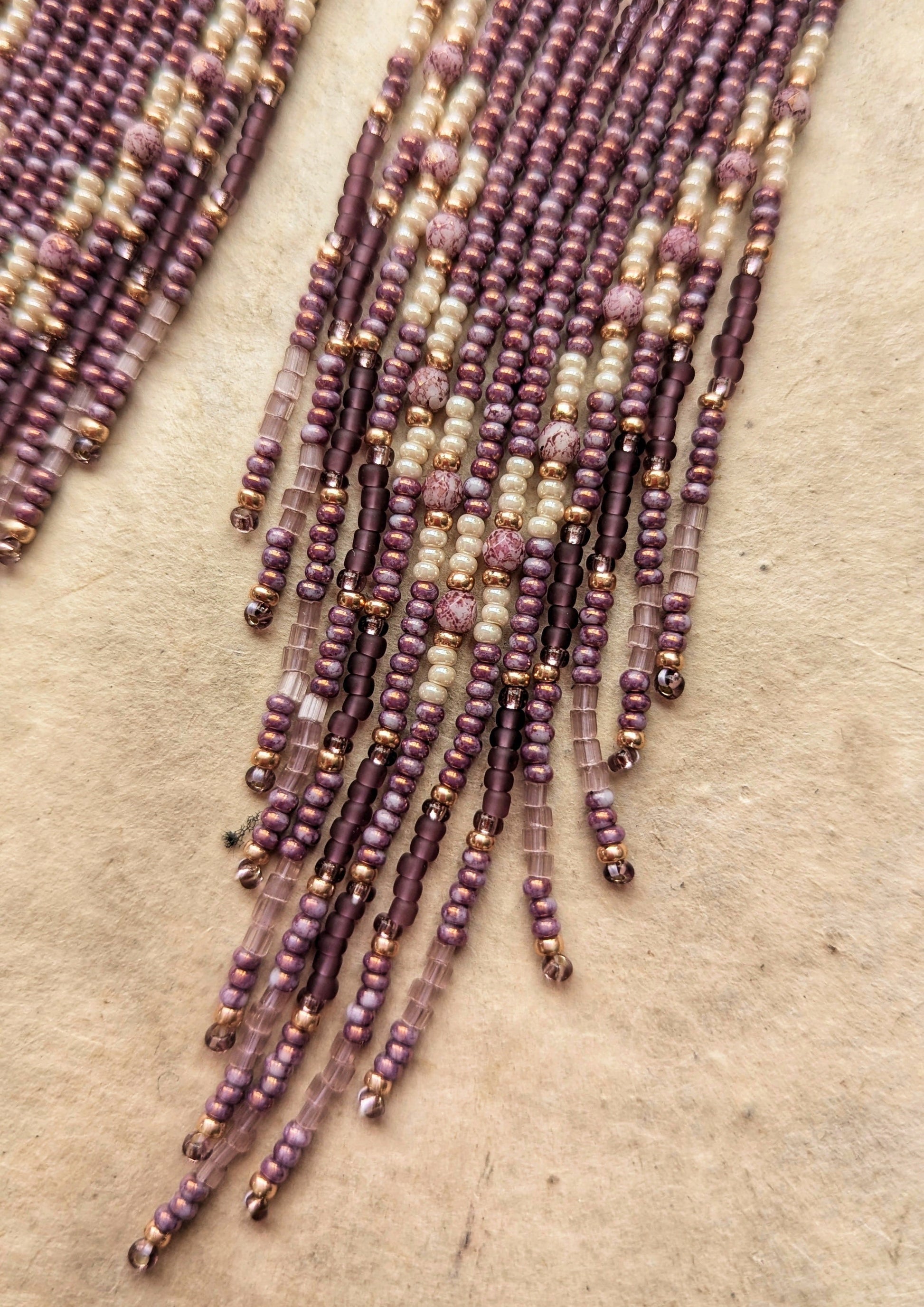 Moon & Milk - close-up of beaded earrings featuring purple and cream strands cascading down, displayed on a neutral background.