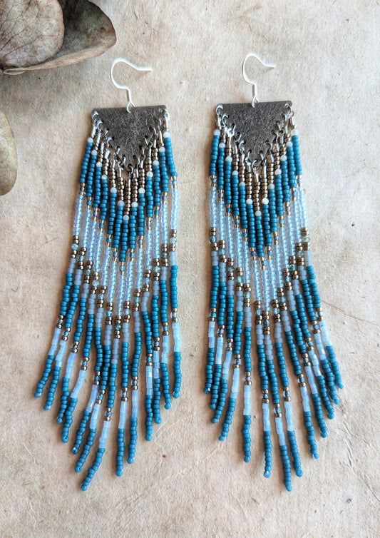 Moon & Milk - Bohemian-style earrings with blue, white, and metallic beads, featuring a long fringe design and a textured silver diamond-shaped top.