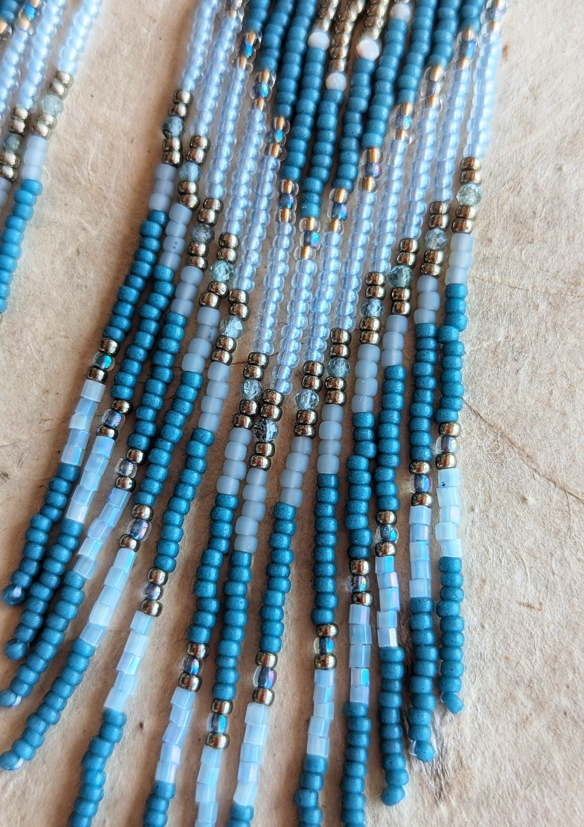 Moon & Milk - a close up of seed bead earrings with blue, white, and metallic beads, featuring a long fringe design.