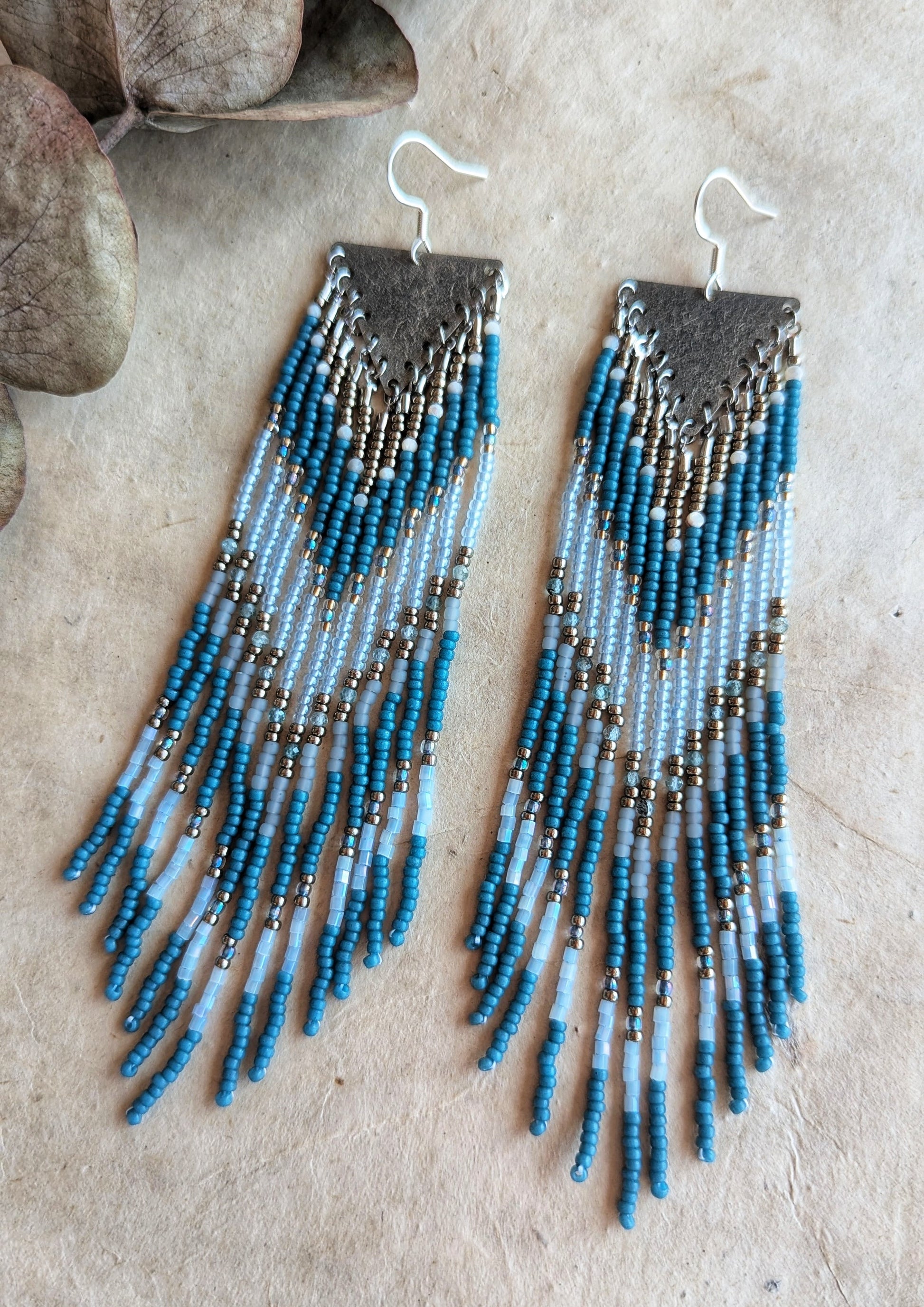 Moon & Milk - Bohemian-style earrings with blue, white, and metallic beads, featuring a long fringe design and a textured silver diamond-shaped top.