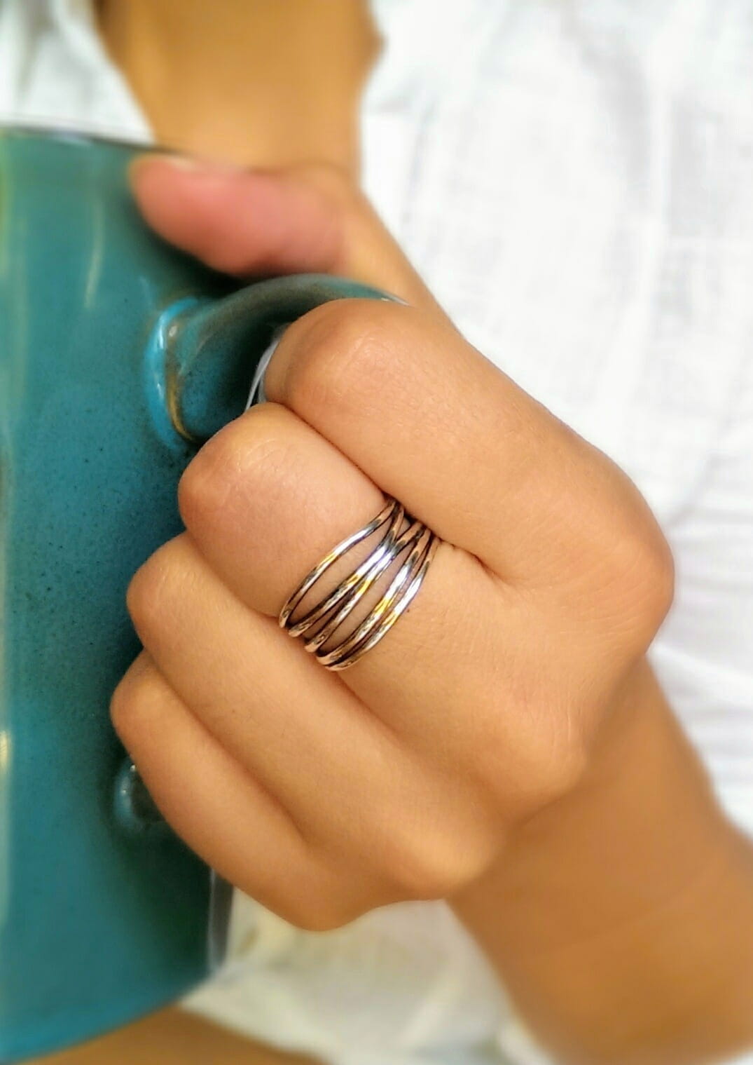 Hand holding a blue mug with a close-up of a silver ring on a blurred background.