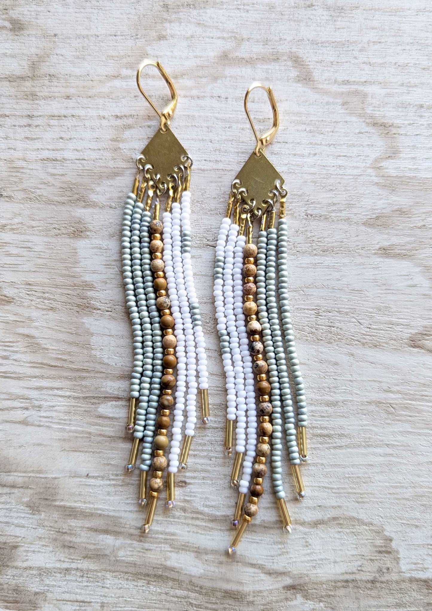 White beaded earrings with gold accents on a wooden surface.