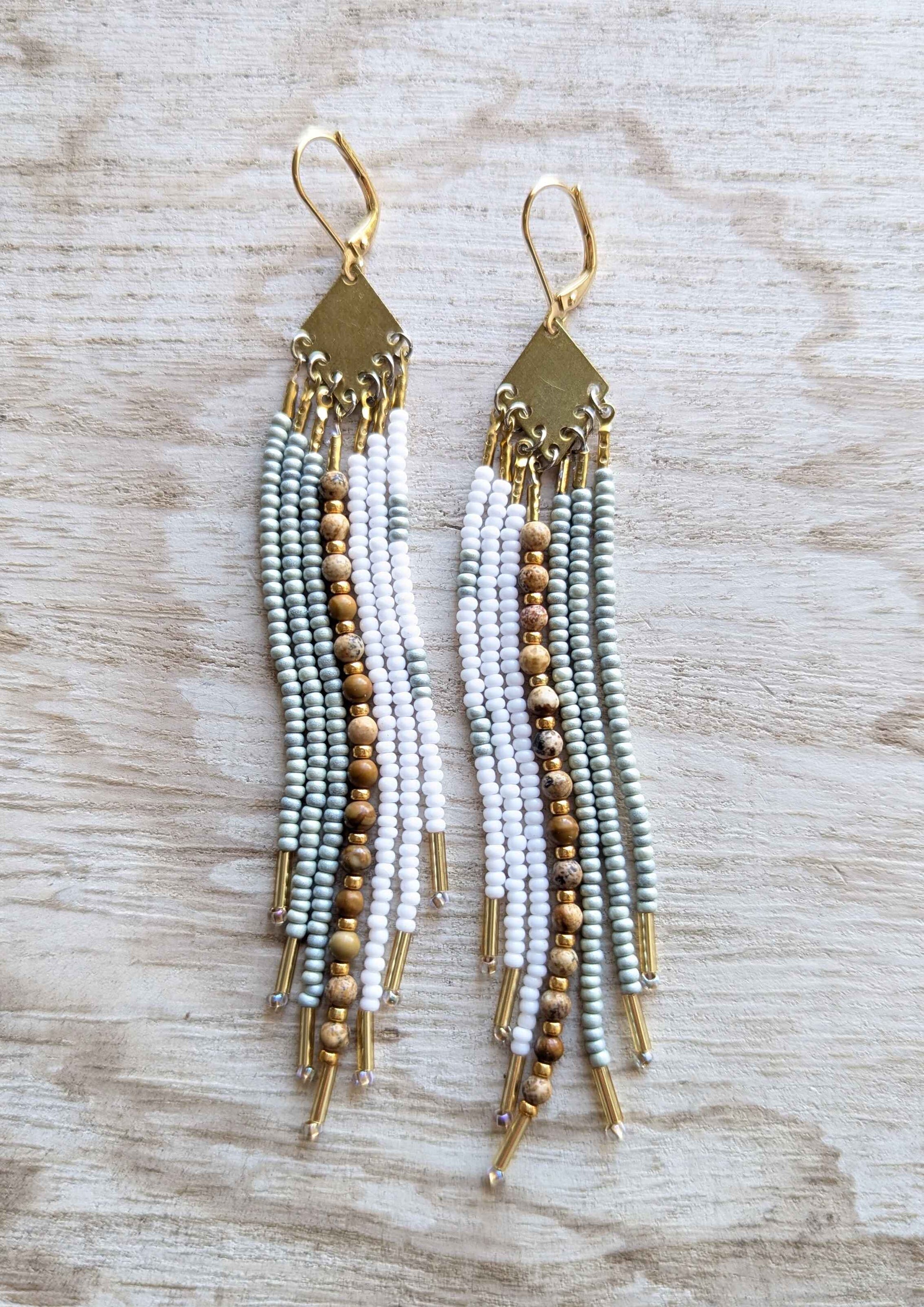 White beaded earrings with gold accents on a wooden surface.