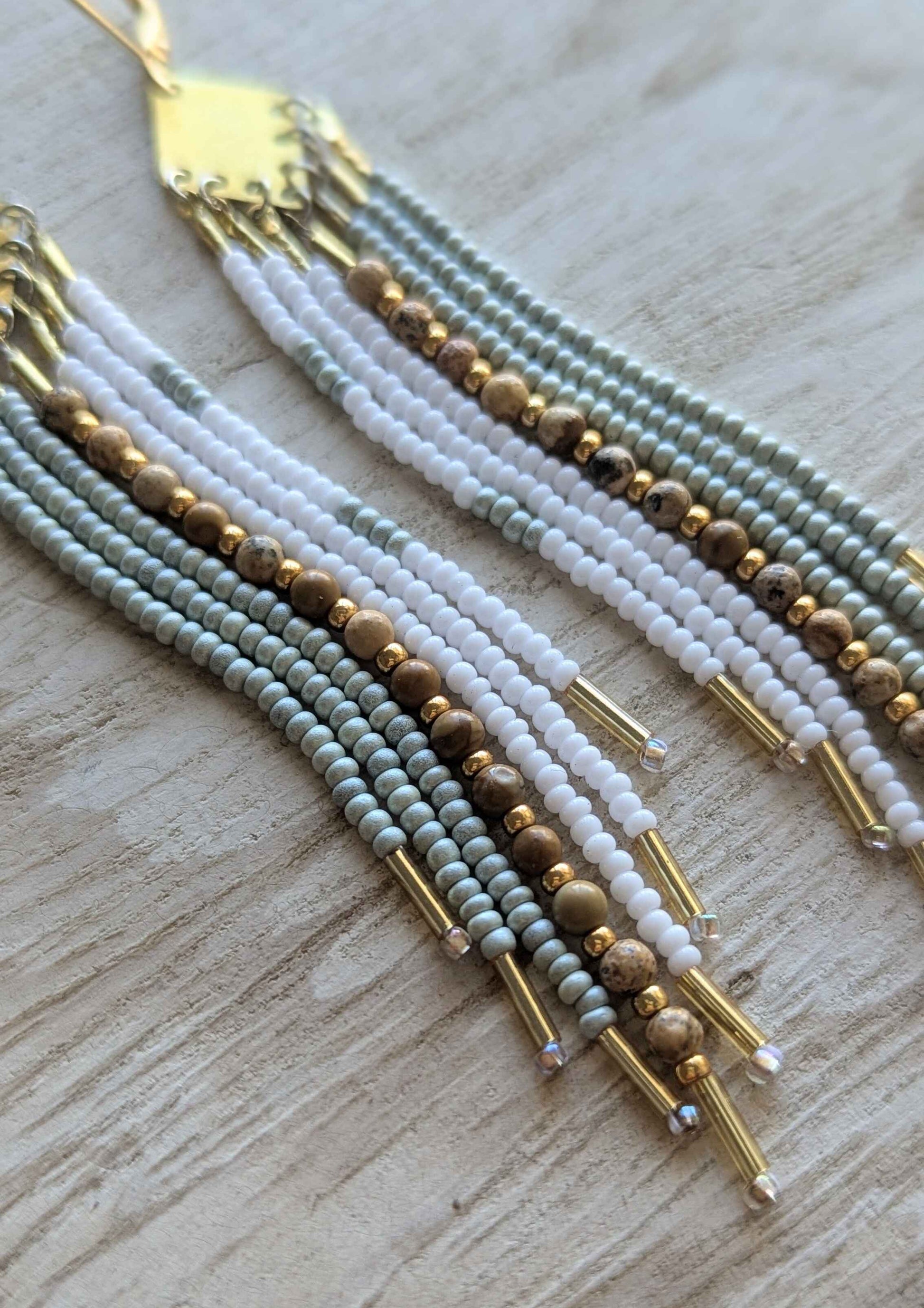 Multistrand beaded earrings with gold accents on a light wooden surface.