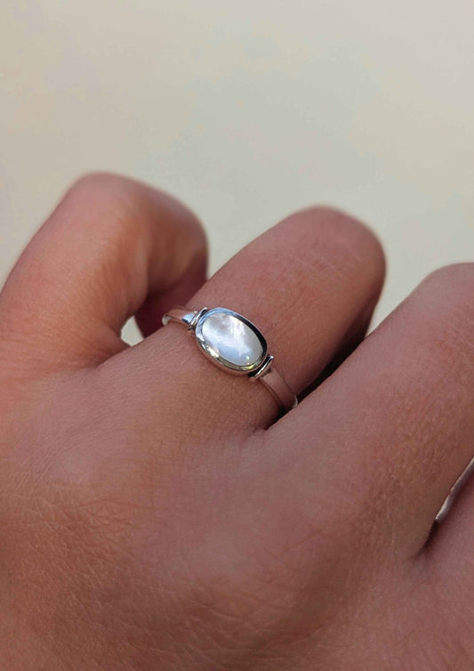 Silver ring with mother-of-pearl on a person's finger against a neutral background.