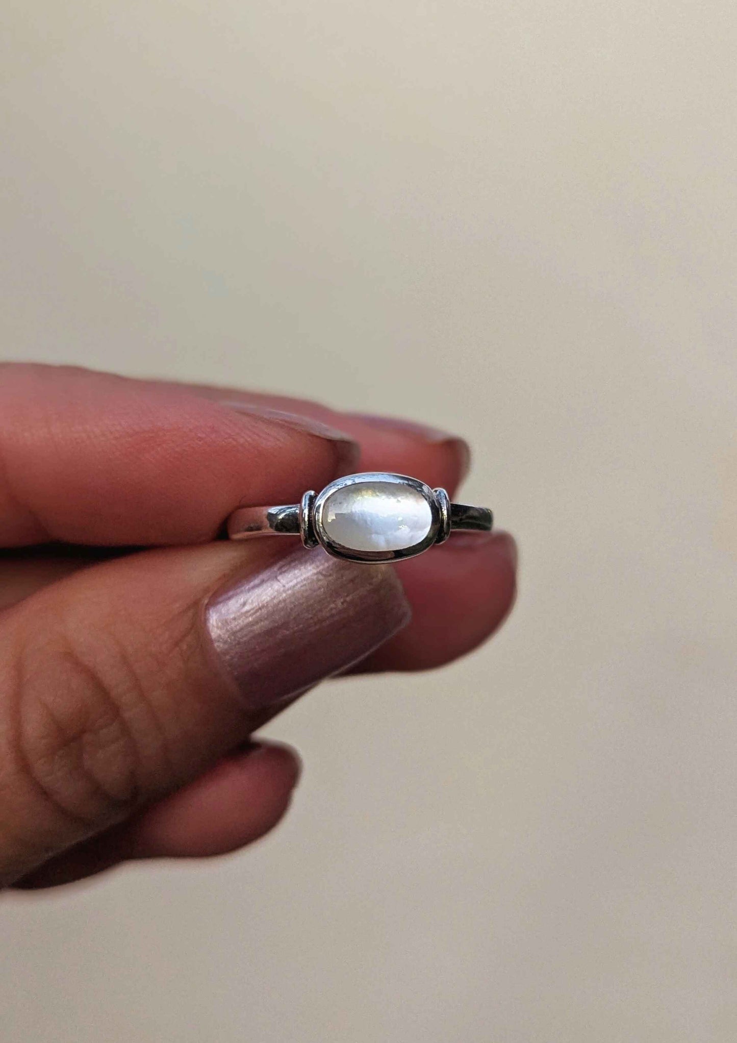 Silver ring with a mother of pearl in the center held between fingers against a plain background.