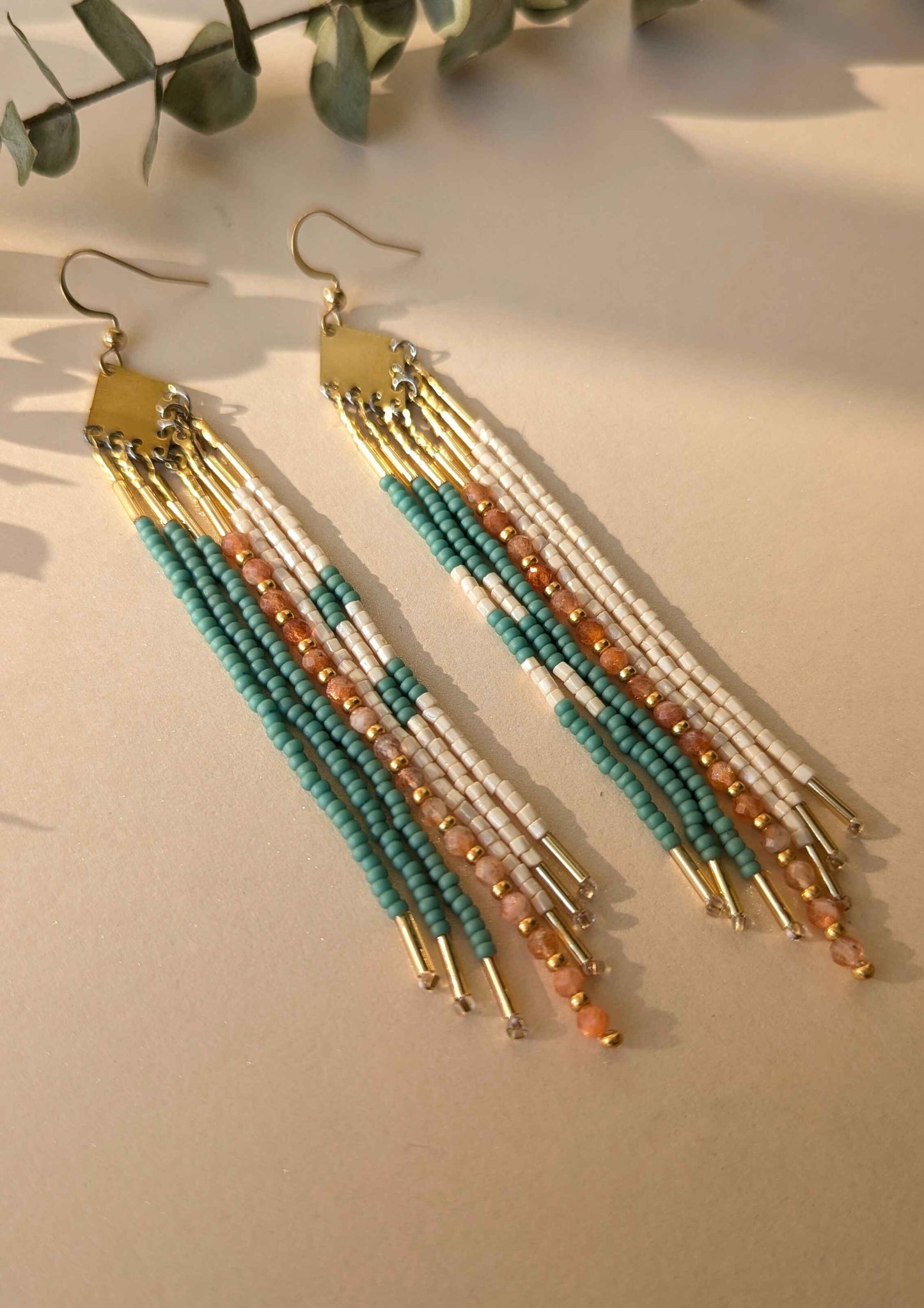 Beaded earrings with gold, turquoise, and sunstone beads on a light background.