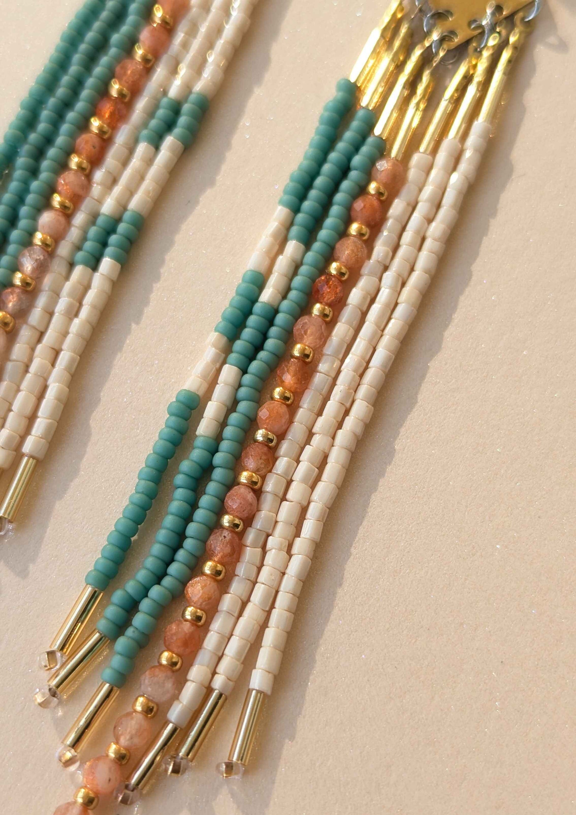 Set of beaded fringes with turquoise, gold, and beige beads on a beige background.