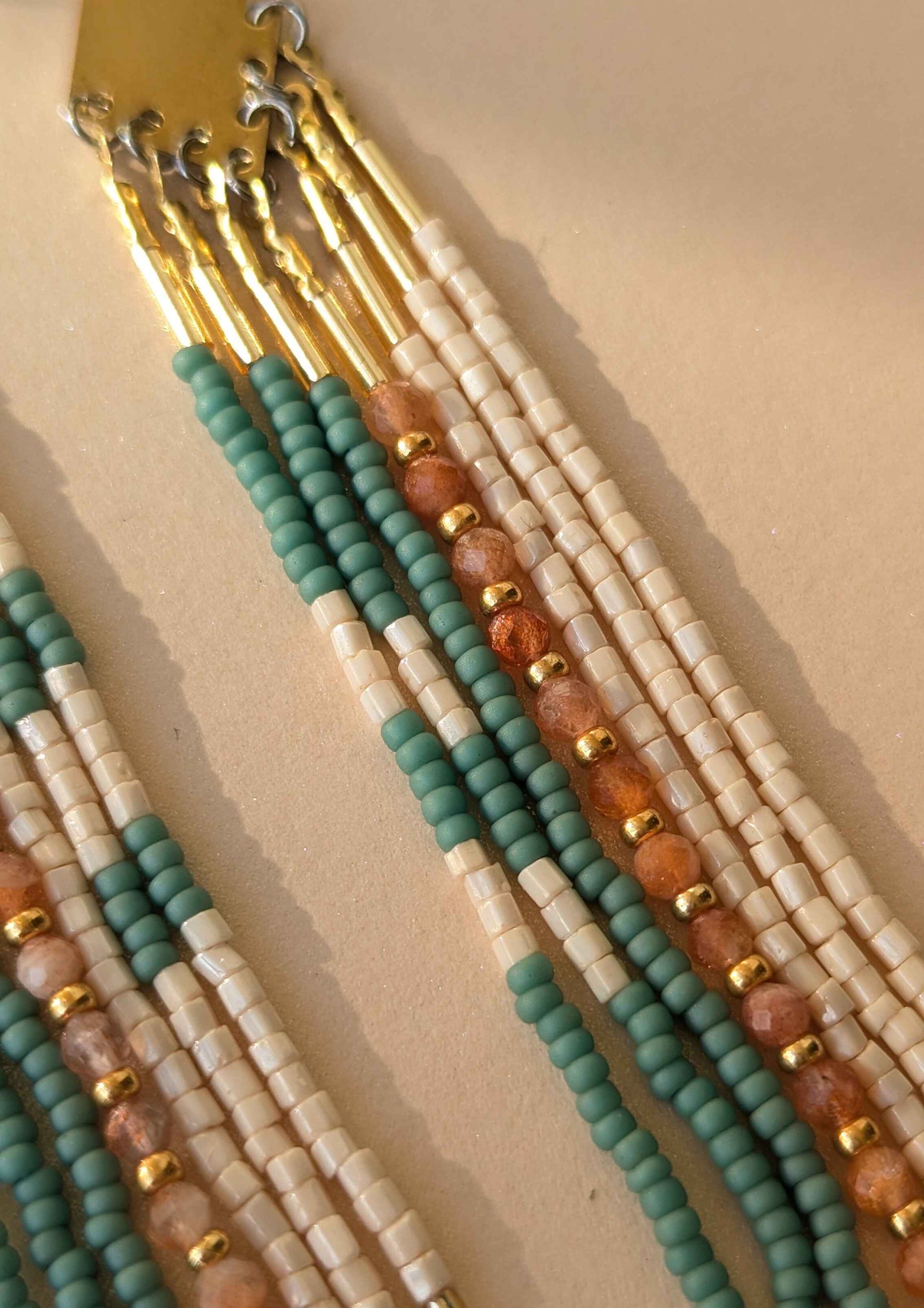 Beaded earrings with gold, green, and sunstone beads on a beige background.