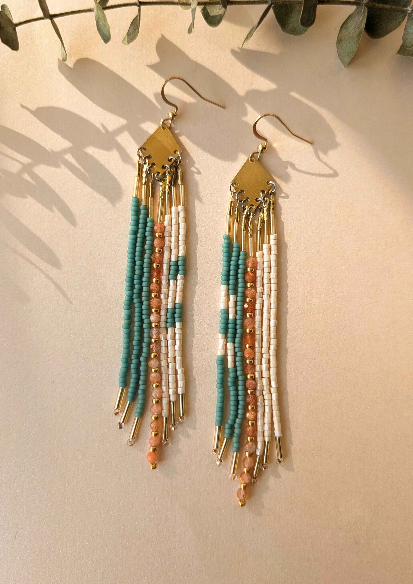 Beaded earrings with sunstone and ivory seed beads on a beige background.