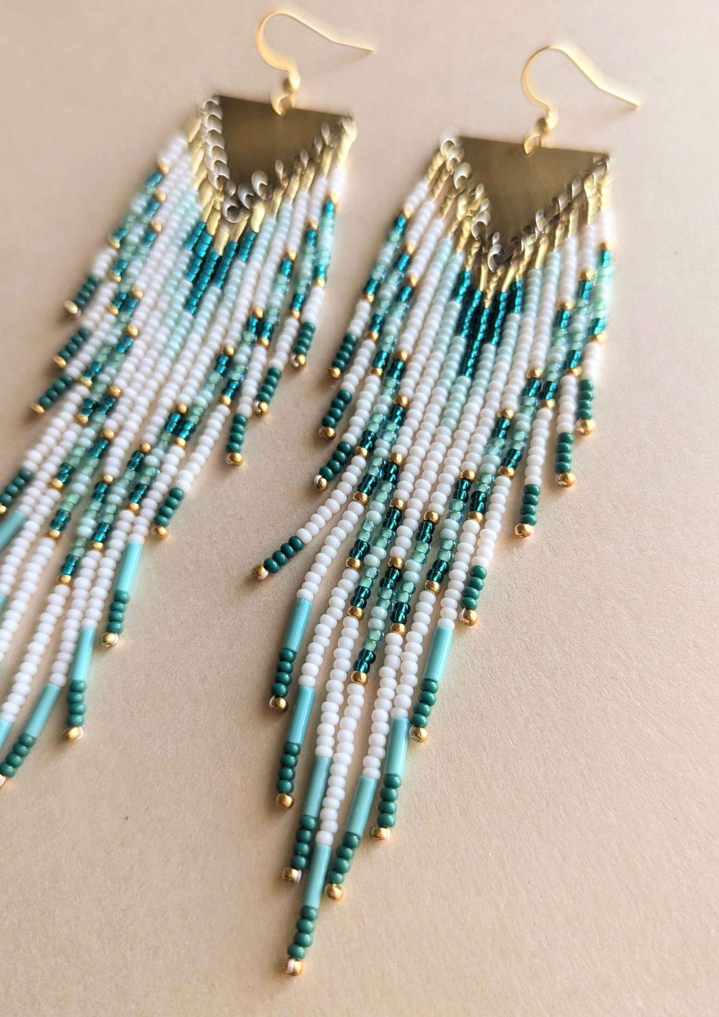 Beaded earrings with teal, turquoise, and white beads on a beige background.