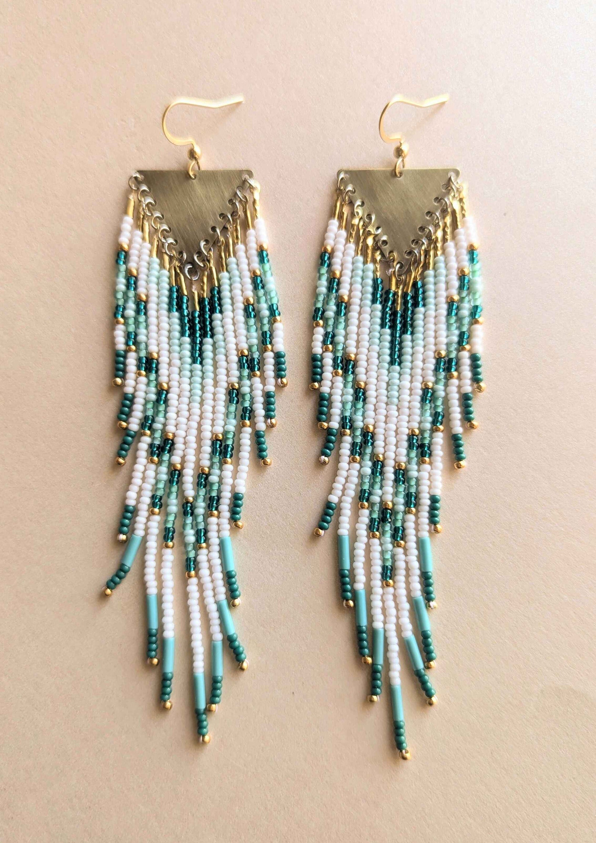 Beaded earrings with turquoise and gold fringes on a beige background.