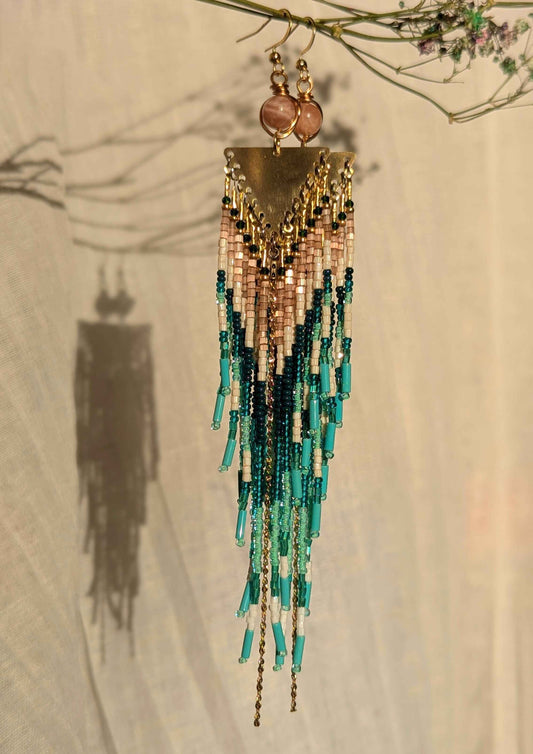 Beaded earrings with gold, green, and pink beads hanging against a neutral background.
