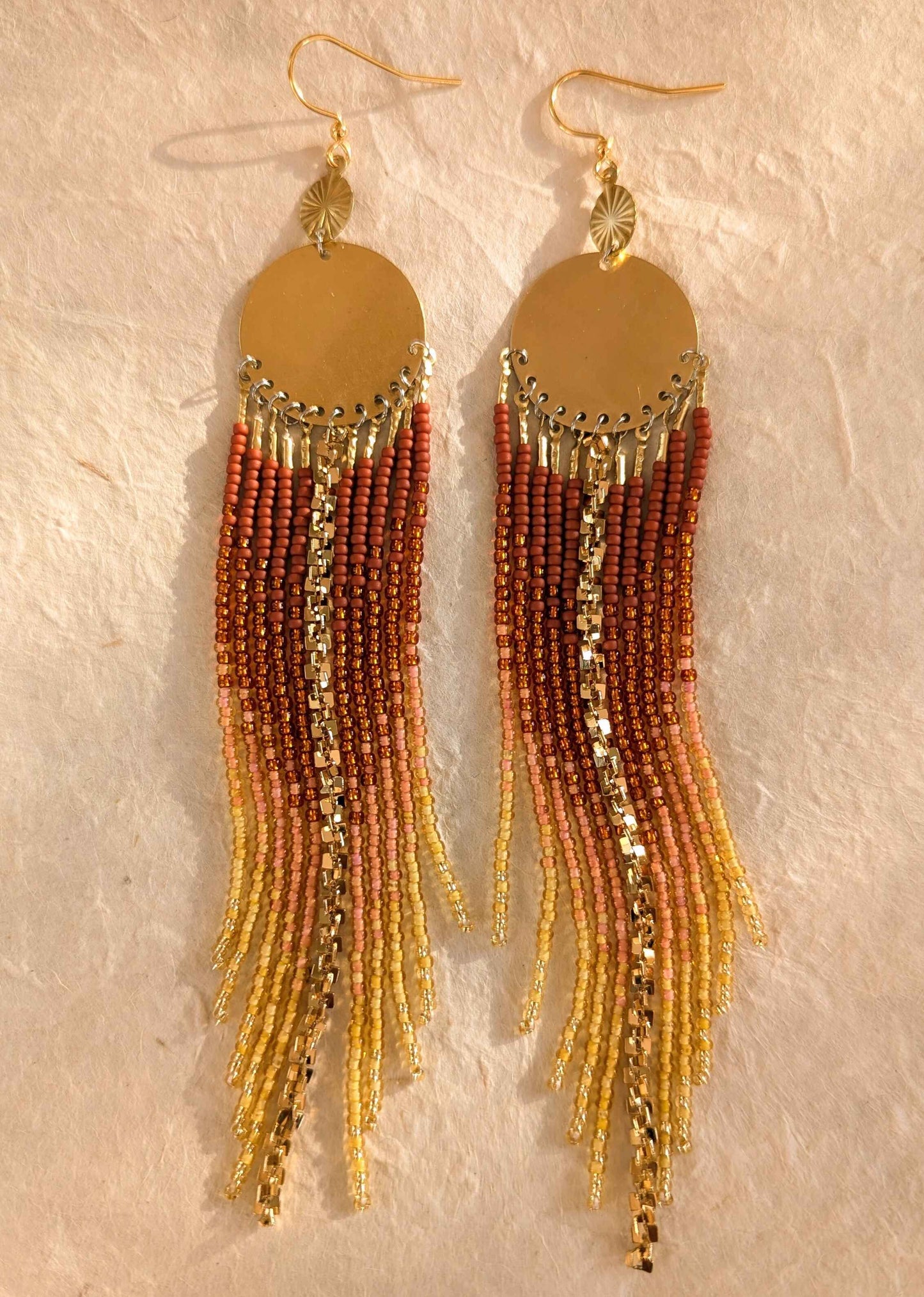 Pair of gold ombre beaded earrings on a textured beige background.