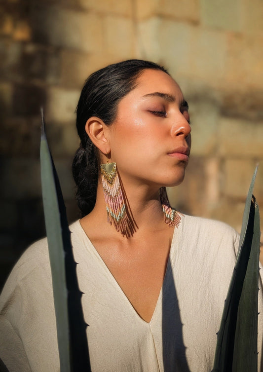 Woman wearing long native earrings against a blurred natural background.