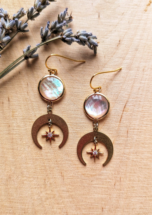 Electra MOP earrings with mother of pearl and CZ star charms, and crescent moon drops in 18k gold-plated brass on a wooden background.