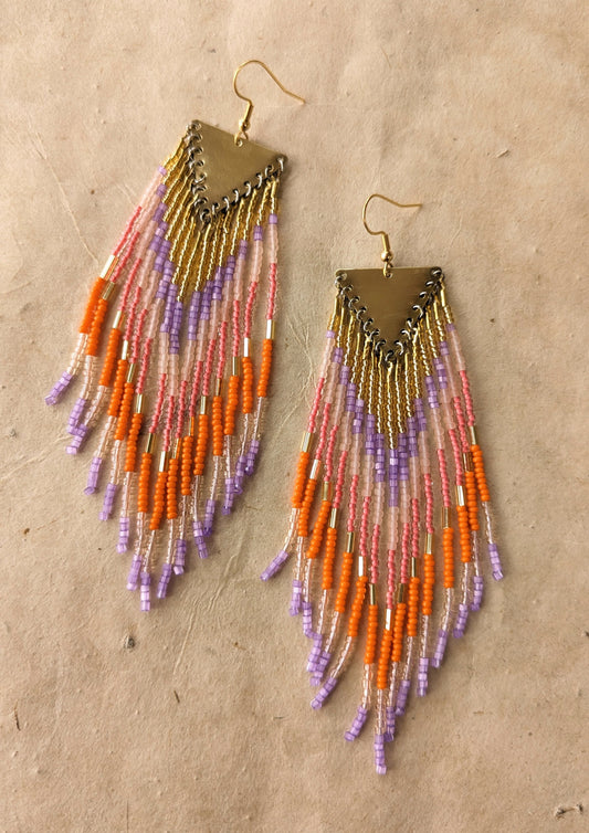 Orange Popsicle earrings by Moon & Milk with orange, lavender, pink, and peach seed beads, handcrafted into long fringe hanging from brass triangle tops.