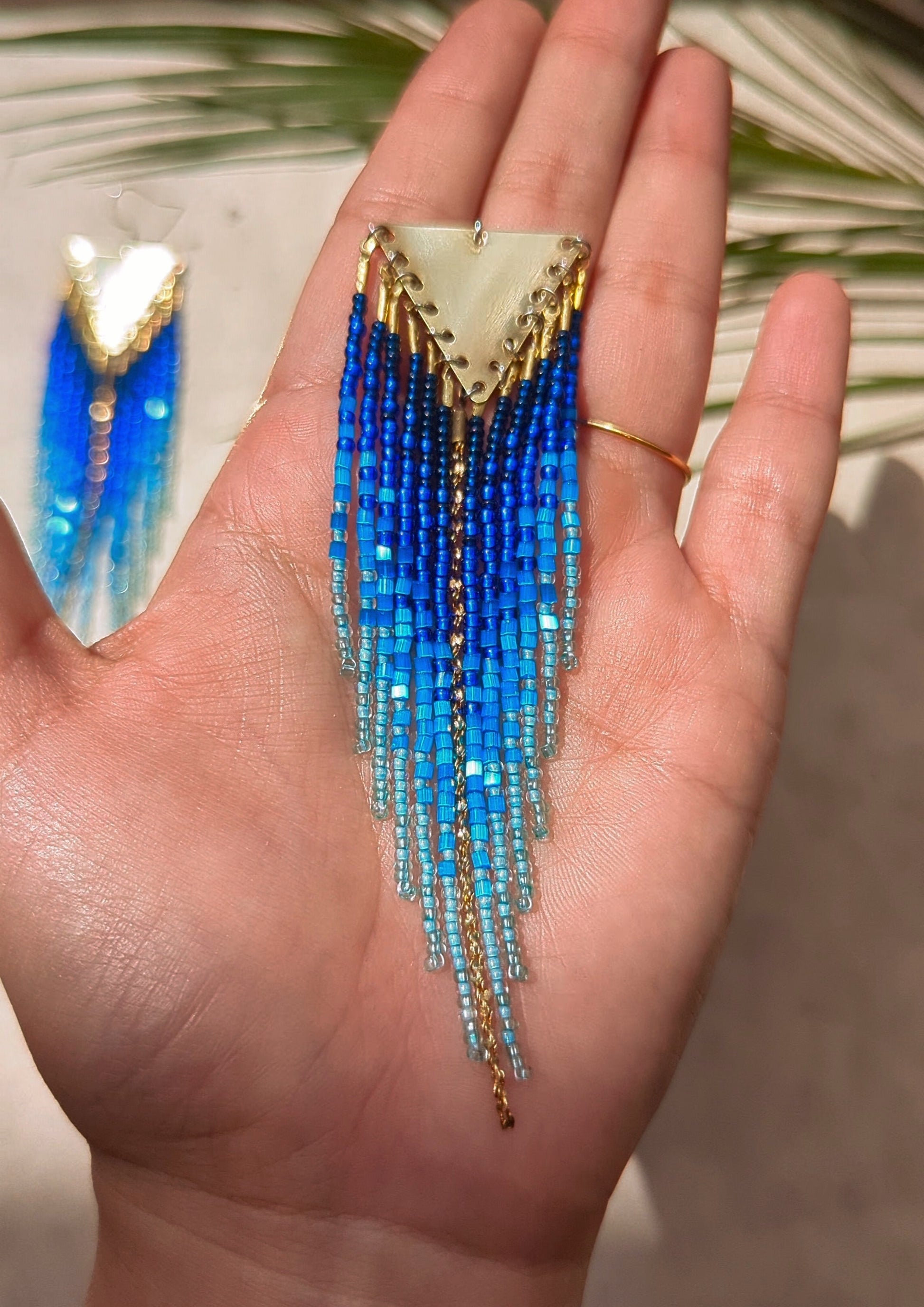 Seed bead earrings with blue and turquoise beaded strands in a gradient pattern. Triangular gold brass metal top.