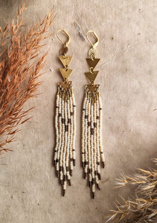 Moon & Milk - Gold triangle-link earrings with cascading cream and bronze seed bead strands, displayed on a neutral background with dried plants for decoration.