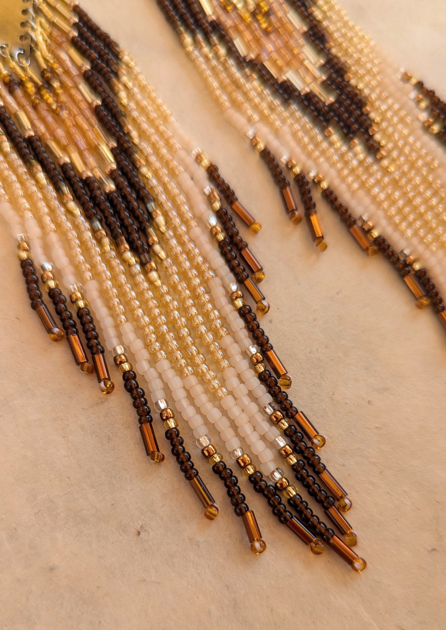 Moon & Milk - Handmade earrings with long brown, gold, and beige bead fringe hanging from a brass plate, creating an earthy and bold design.