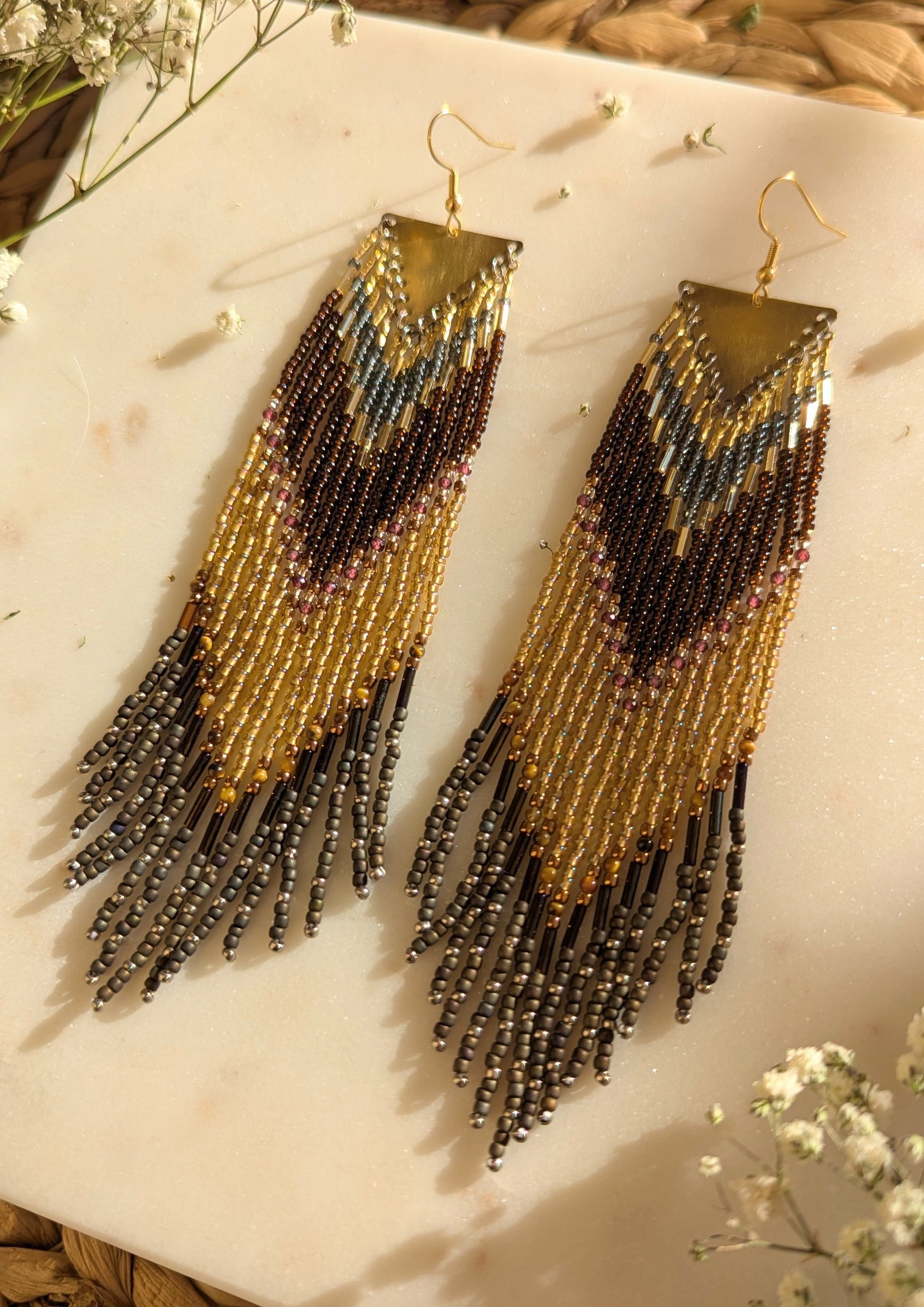 Chevron-patterned beaded earrings in gold, brown, and rustic tones with fringe details, handcrafted for a boho-chic and elegant statement.