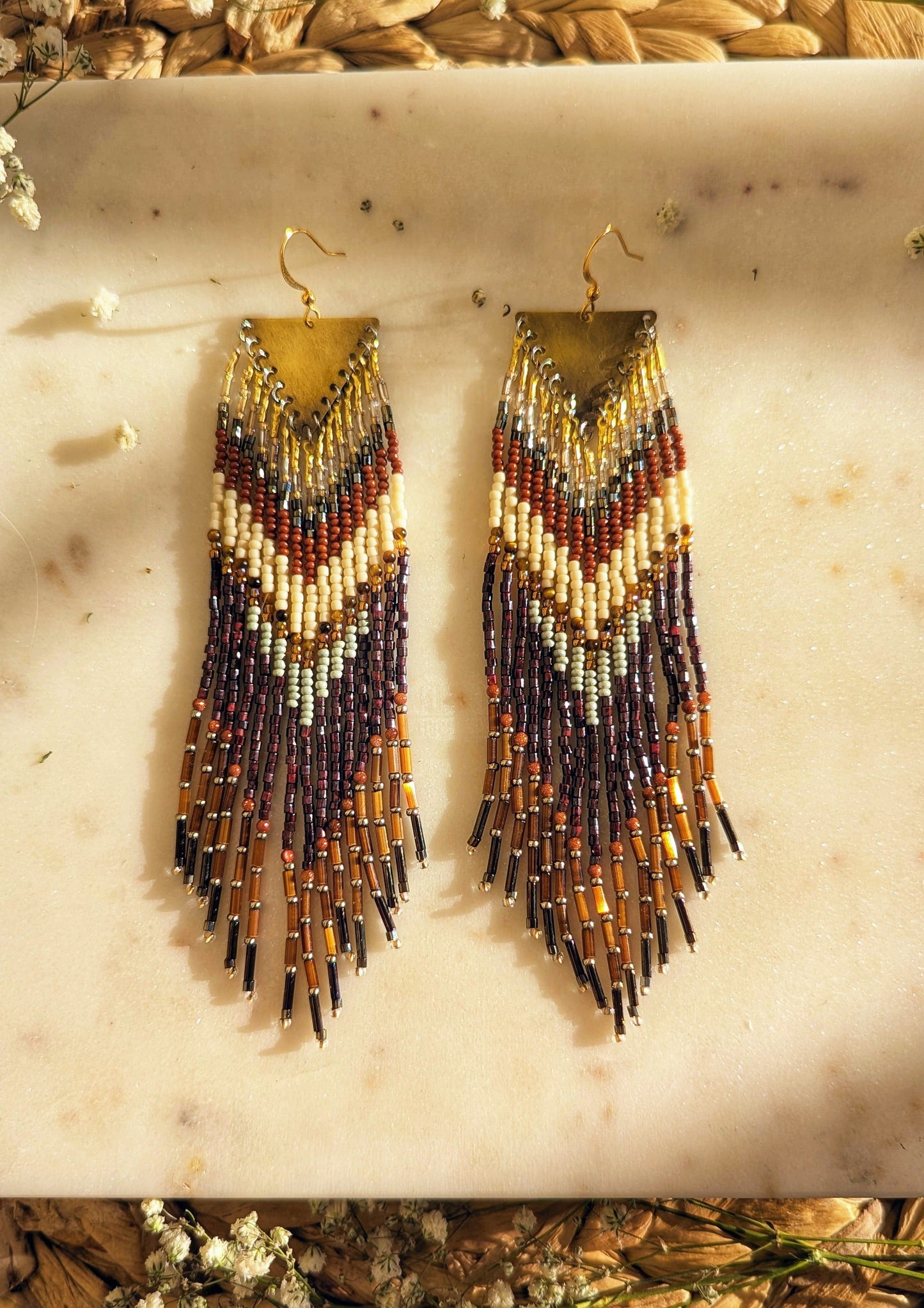 Handcrafted beaded fringe earrings with a chevron pattern in earthy tones of burgundy, gold, cream, and mint, accented by fringe with metallic gold and black details.