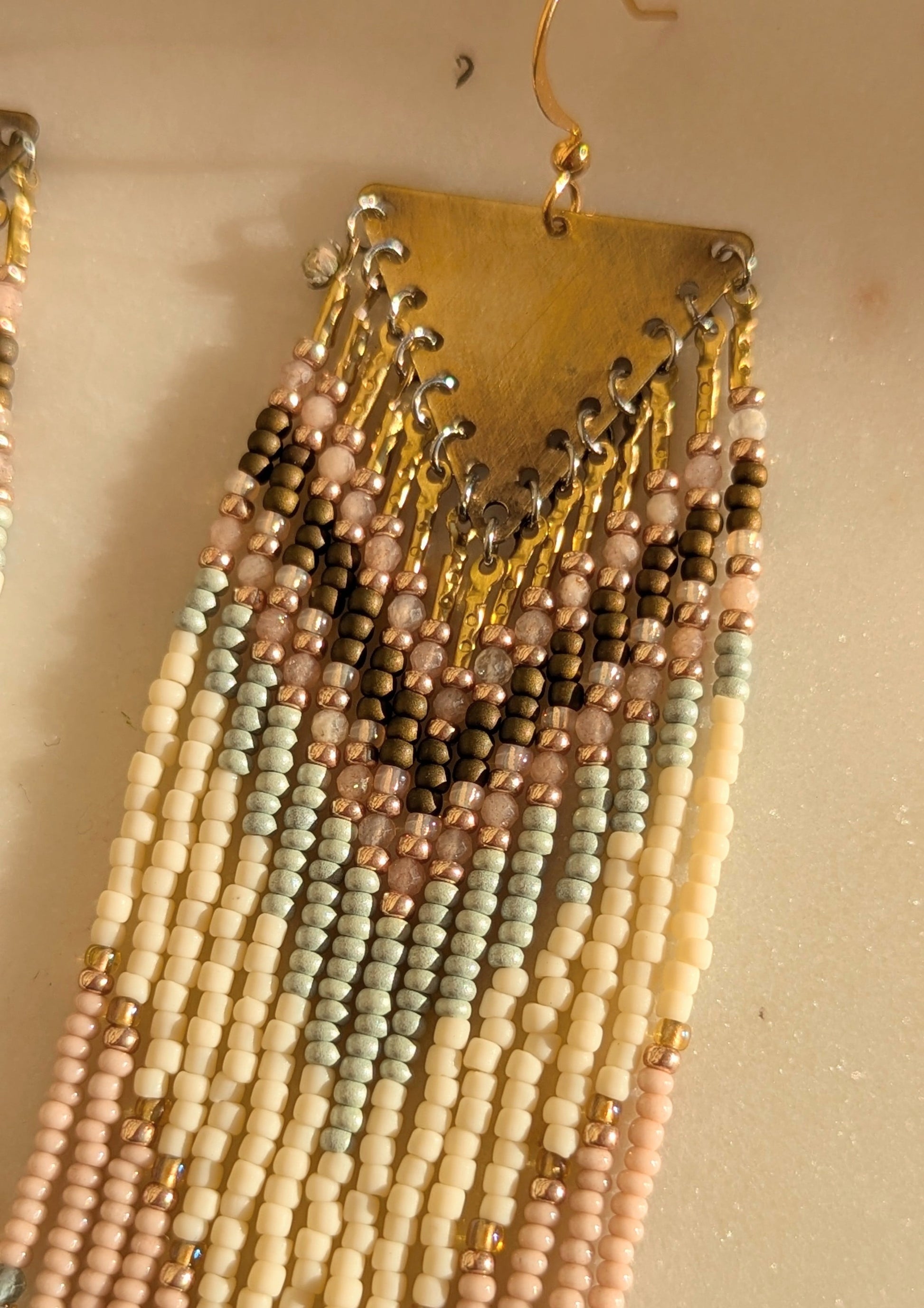 Delicate beaded fringe earrings with pastel tones of cream, blush, and mint green in a chevron pattern, finished with shimmering bronze fringe accents.