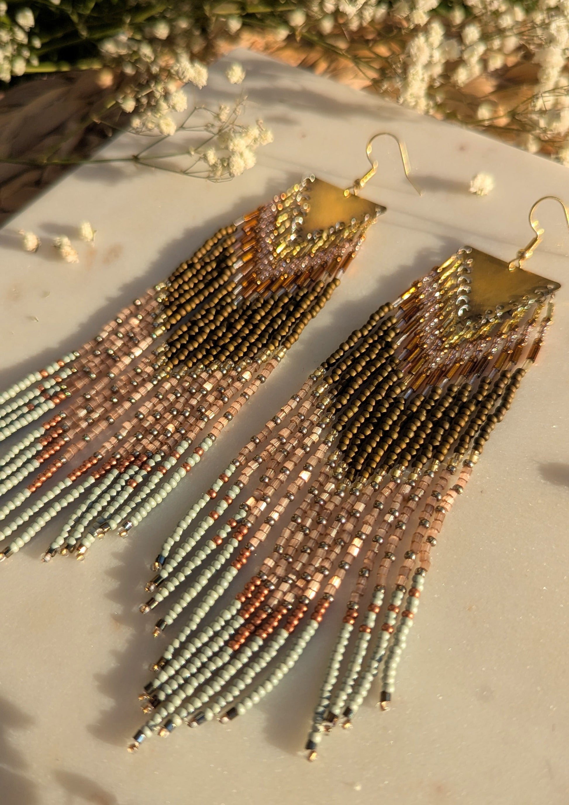 Handcrafted beaded fringe earrings with a chevron pattern in gold, bronze, and mint green, accented by delicate fringe and shimmering details.