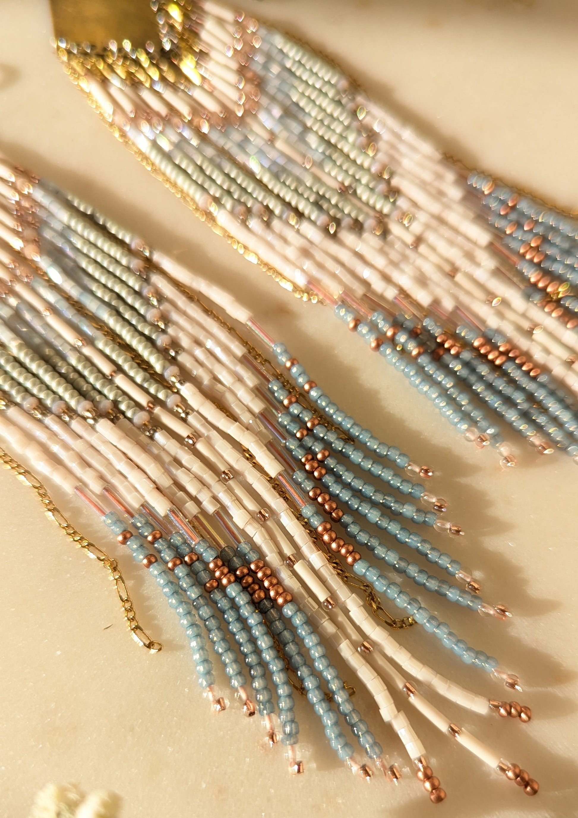 Handcrafted beaded fringe earrings featuring a chevron pattern in pastel blue, ivory, and gold, with cascading beaded fringes for a bohemian-inspired look.