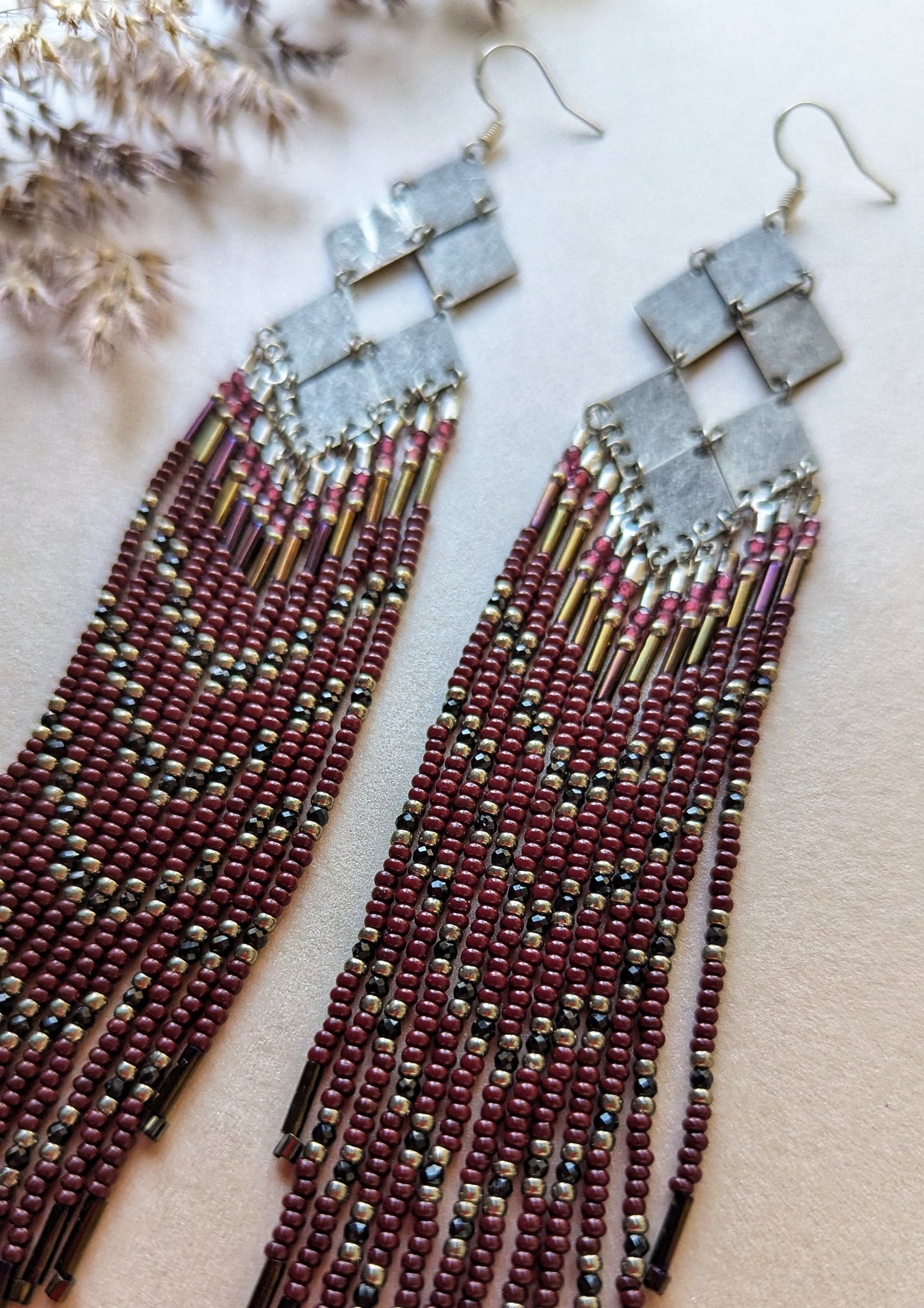 Handcrafted beaded earrings with geometric silver accents, burgundy beads, and intricate fringe design, perfect for boho or evening wear styles.