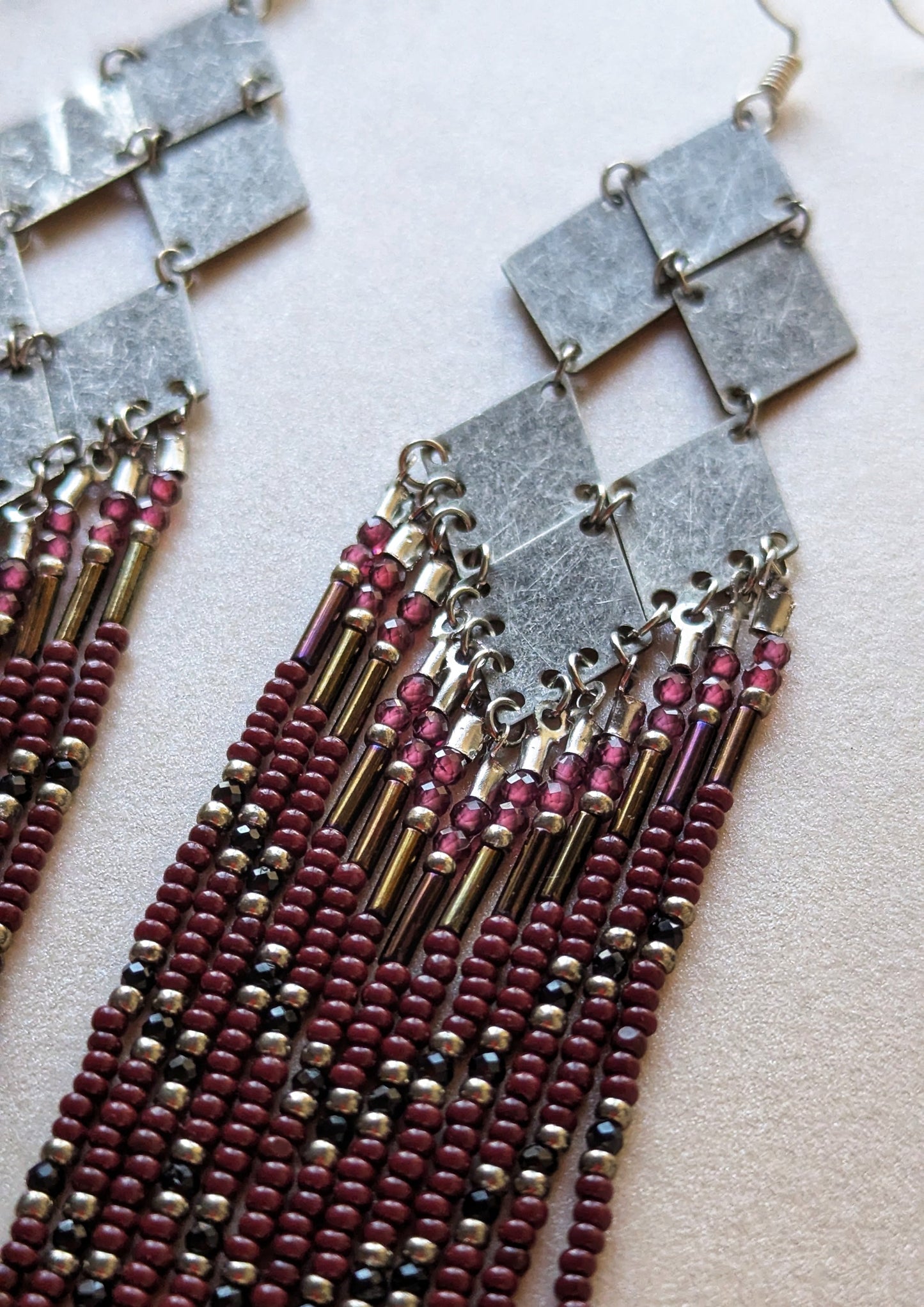 Handcrafted beaded earrings with geometric silver accents, burgundy beads, and intricate fringe design, perfect for boho or evening wear styles.