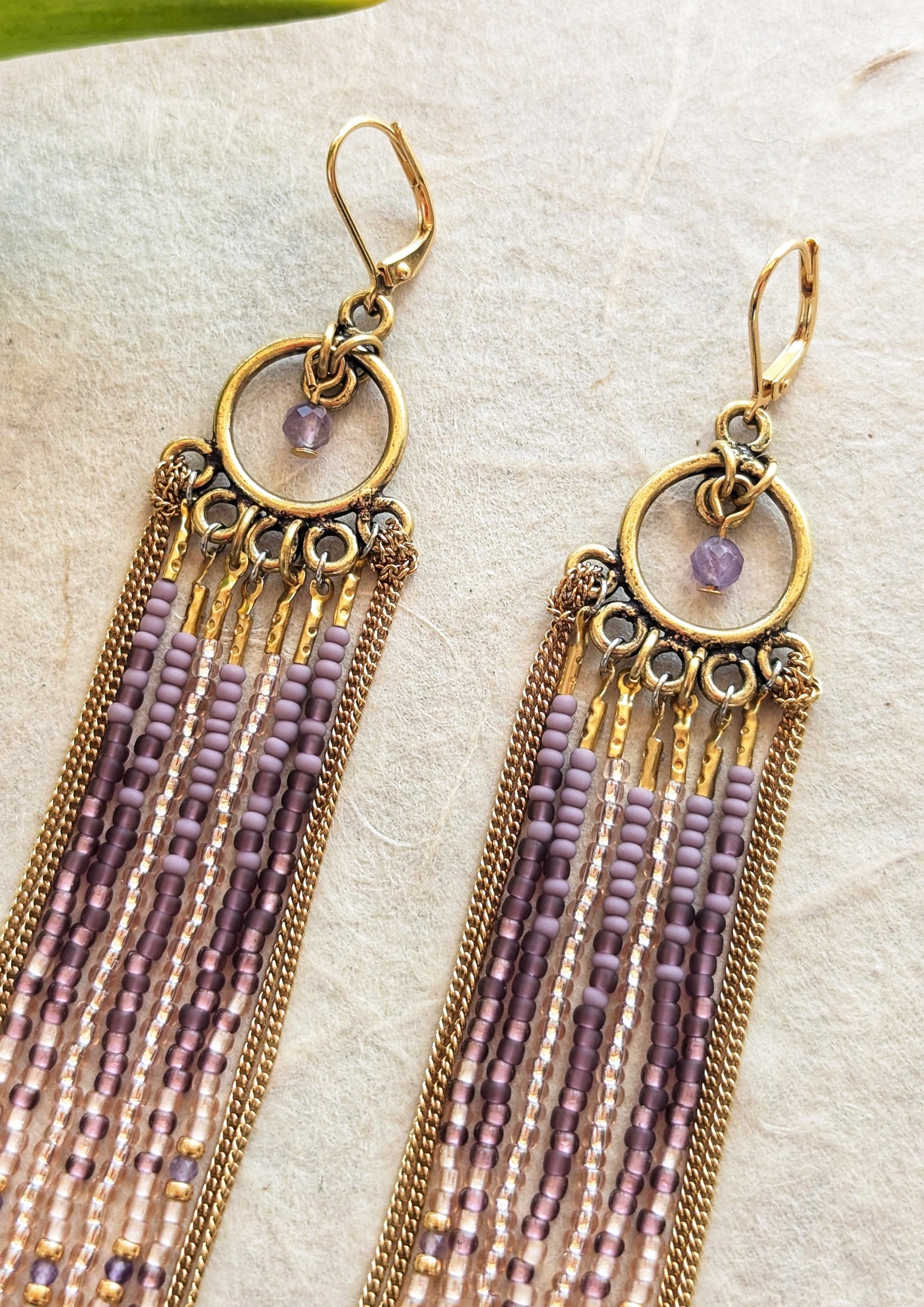 Moon & Milk handcrafted beaded earrings with glass beads in lilac and mauve tones, amethyst natural stones, accented by brass chain fringe in a long artisan earring design.