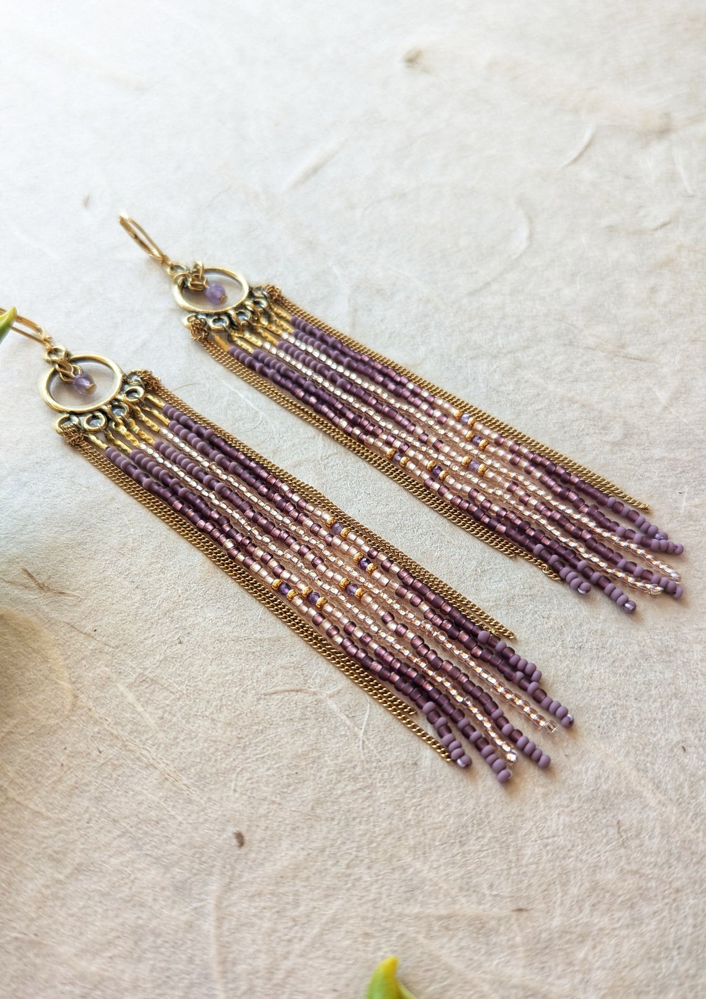 Moon & Milk handcrafted beaded earrings with glass beads in lilac and mauve tones, amethyst natural stones, accented by brass chain fringe in a long artisan earring design.
