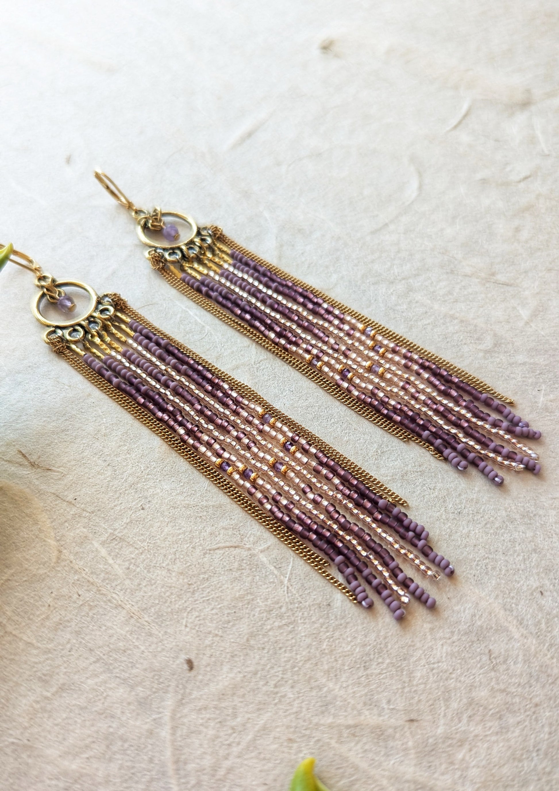 Moon & Milk handcrafted beaded earrings with glass beads in lilac and mauve tones, amethyst natural stones, accented by brass chain fringe in a long artisan earring design.
