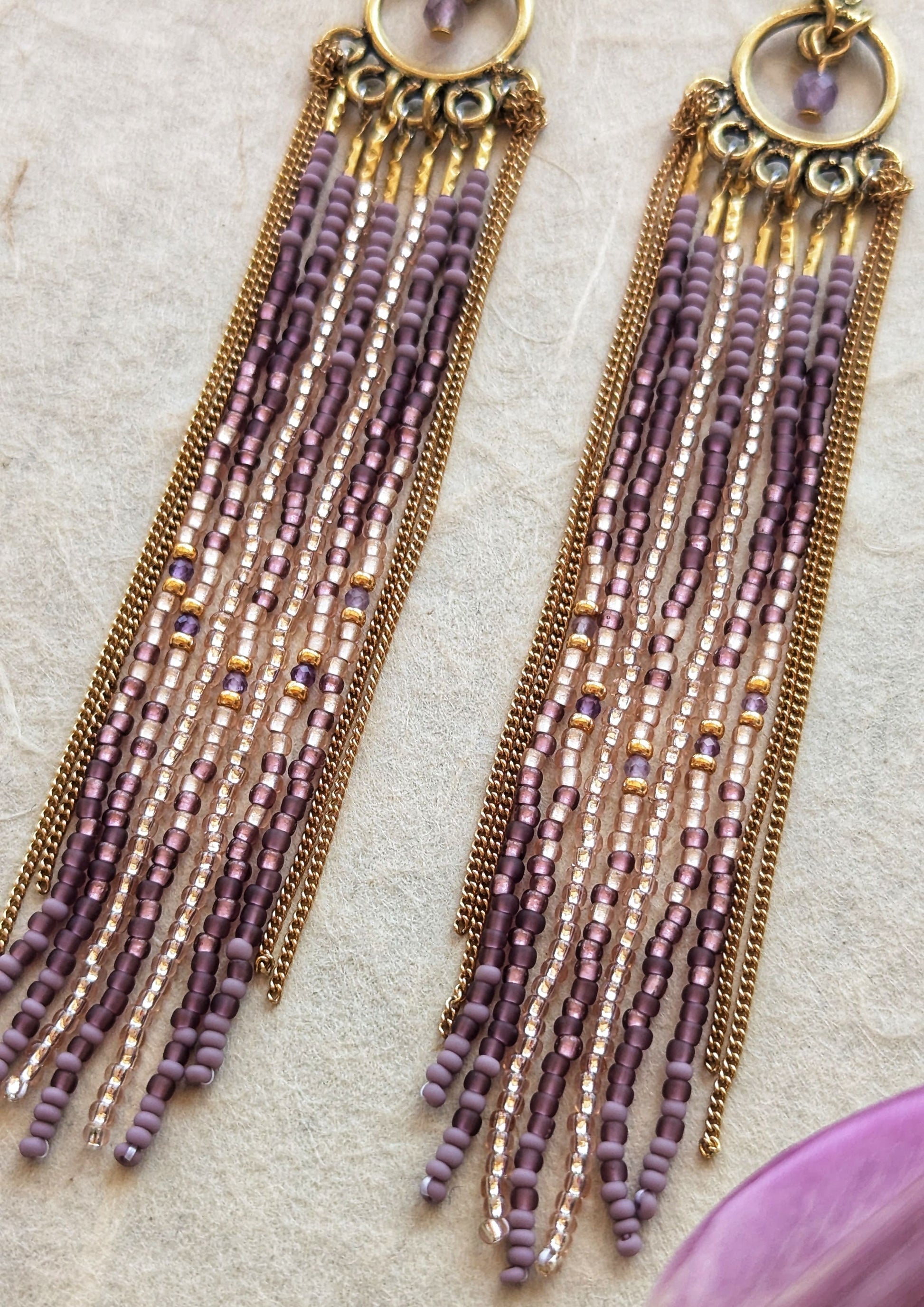 Moon & Milk handcrafted beaded earrings with glass beads in lilac and mauve tones, amethyst natural stones, accented by brass chain fringe in a long artisan earring design.