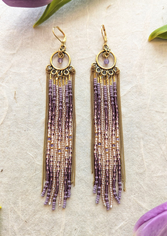 Moon & Milk handcrafted beaded earrings with glass beads in lilac and mauve tones, amethyst natural stones, accented by brass chain fringe in a long artisan earring design.